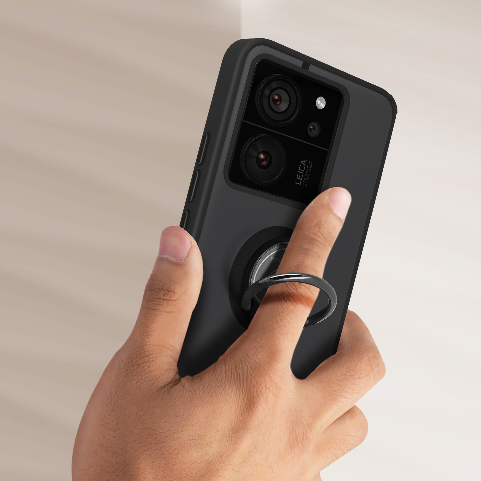 Une coque de smartphone noire avec un porte-anneau, tenue par une main, avec un arrière-plan flou.