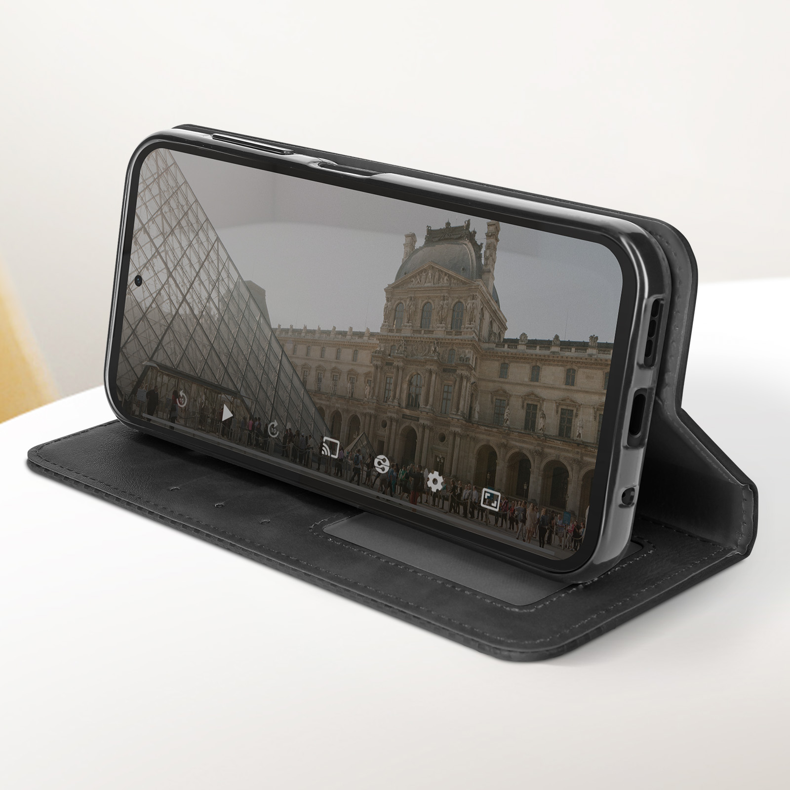 Smartphone che mostra il Museo del Louvre su custodia nera, aperto su superficie bianca.