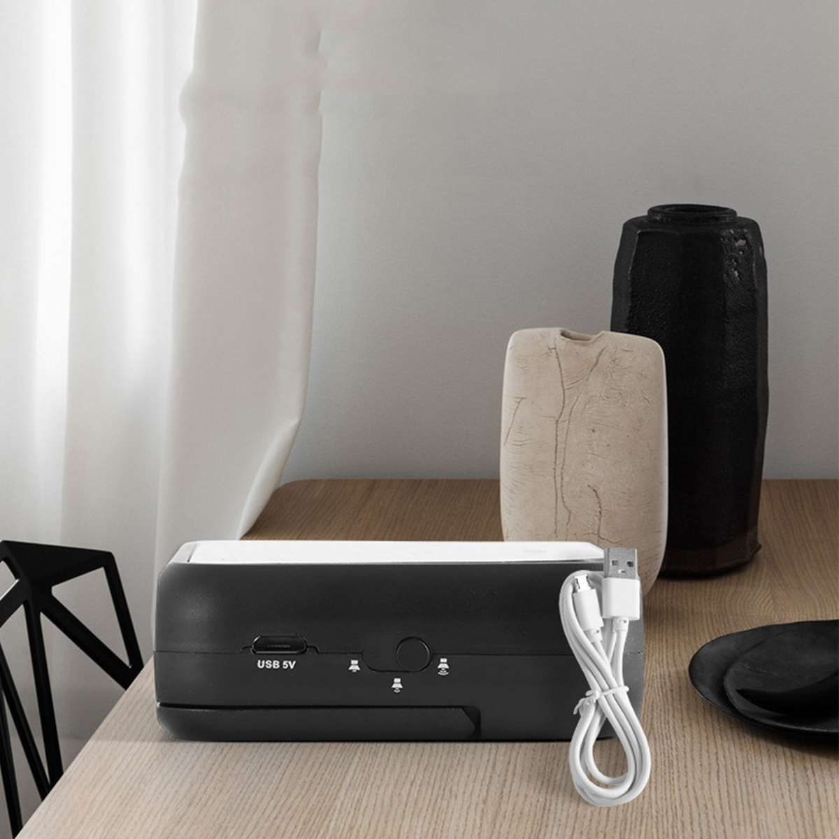 Schwarze und weiße Box mit USB-Kabel und anderen Gegenständen auf einem Holztisch.