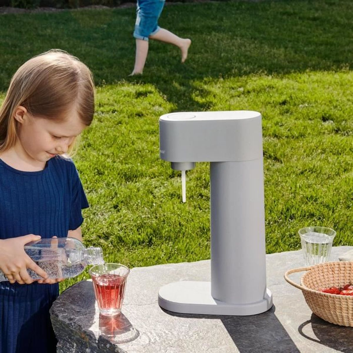 Ein Mädchen gießt Wasser aus einer Flasche in ein Glas, im Hintergrund ein Wasserspender.