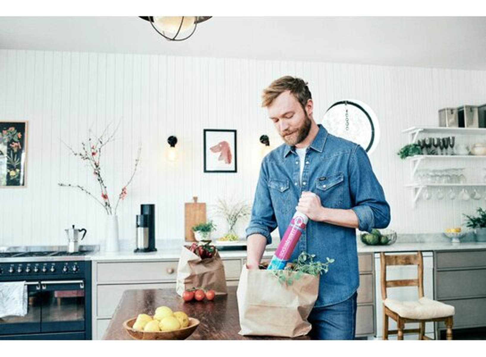 Un uomo con una camicia di jeans mette oggetti in un sacchetto di carta in una cucina.