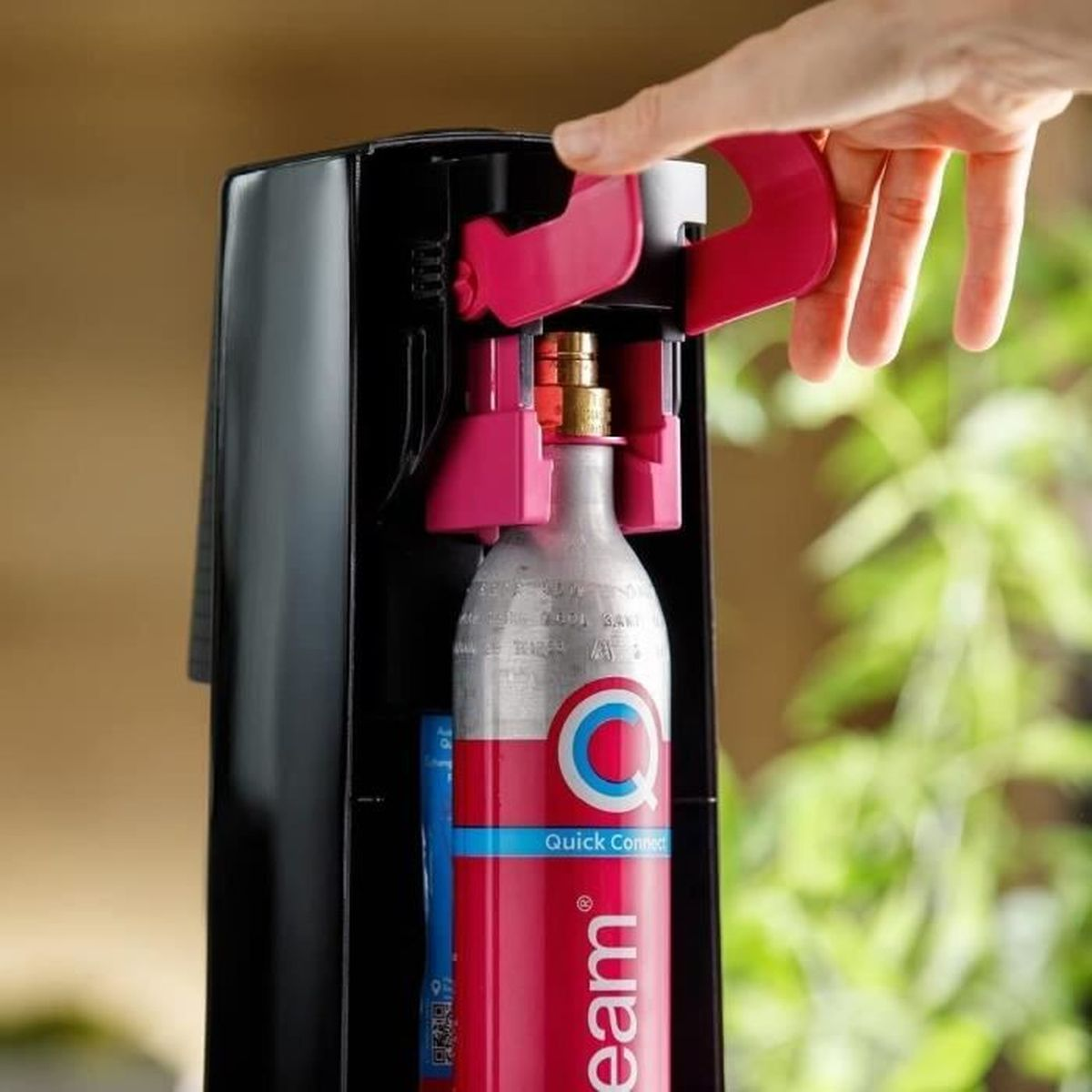 La mano di una persona aziona un produttore di soda nero e rosso con un cilindro rosa.