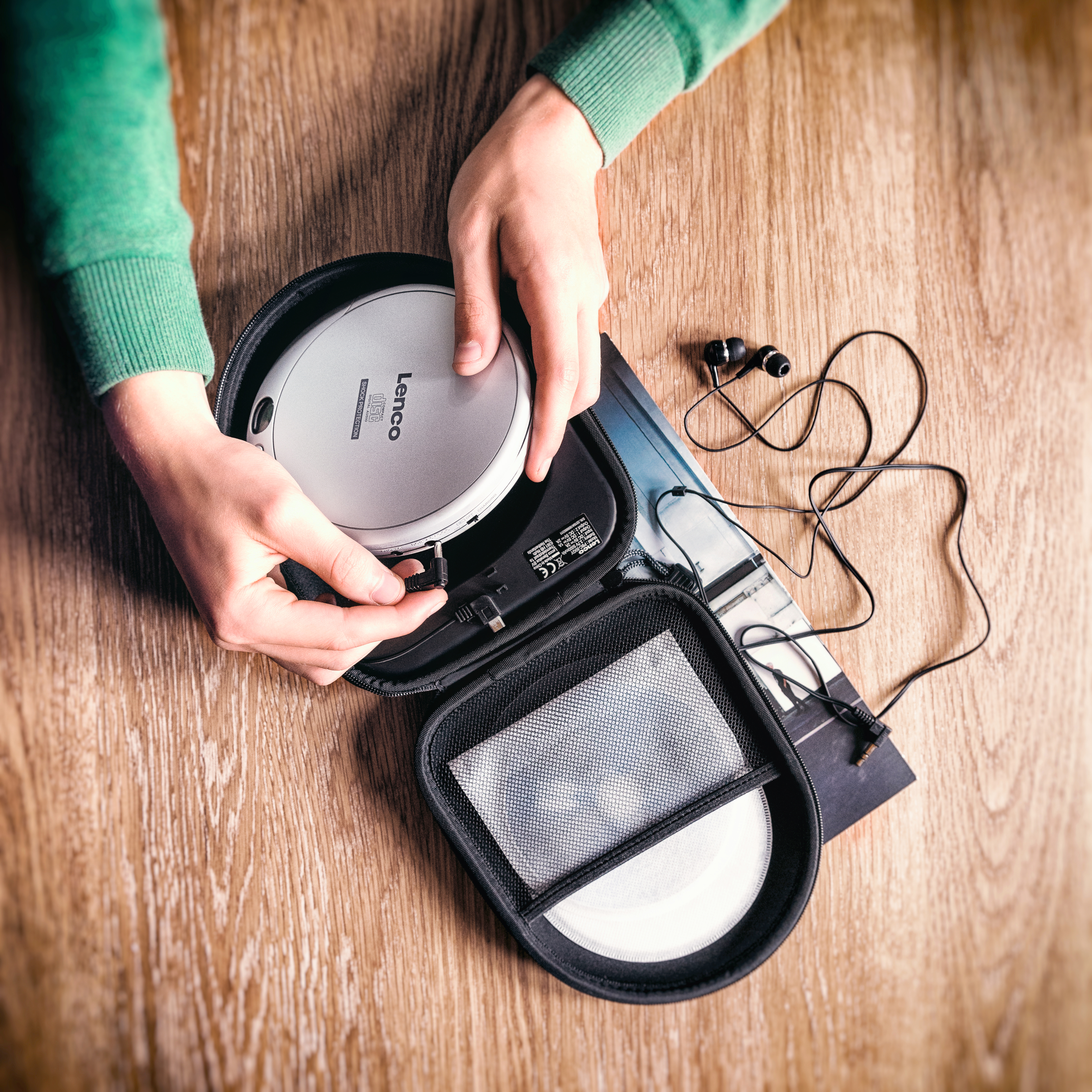 Mains ouvrant un étui de lecteur CD sur bois, avec écouteurs et CD.