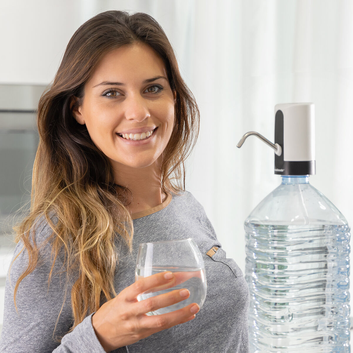 Donna sorridente, tiene un bicchiere d'acqua. Erogatore d'acqua sullo sfondo.