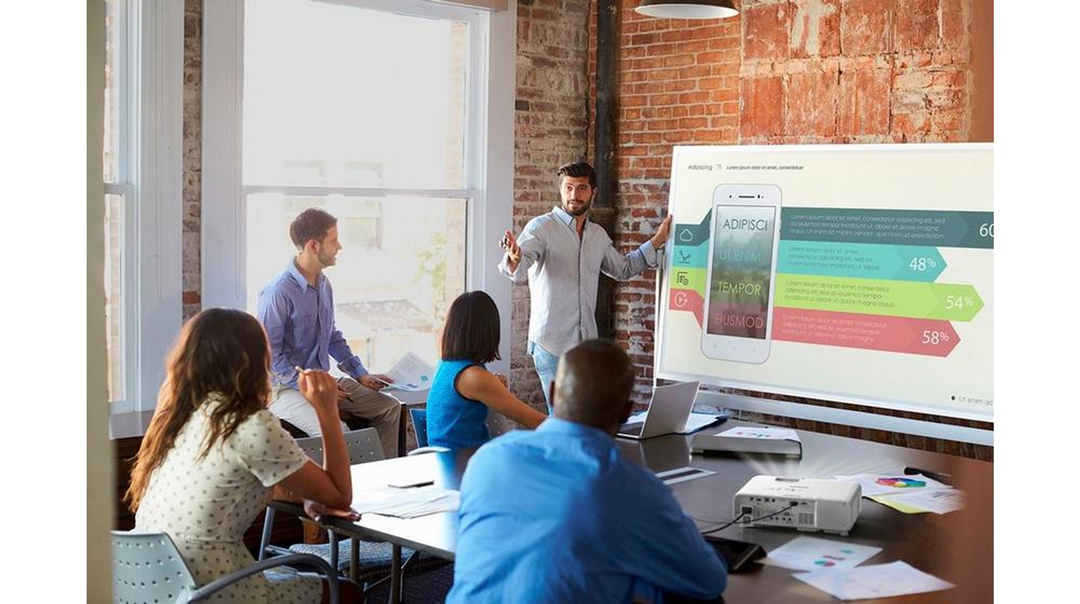 Spotkanie biznesowe z mężczyzną prezentującym wykres na ekranie. Ludzie siedzą przy stole w jasnym pokoju.