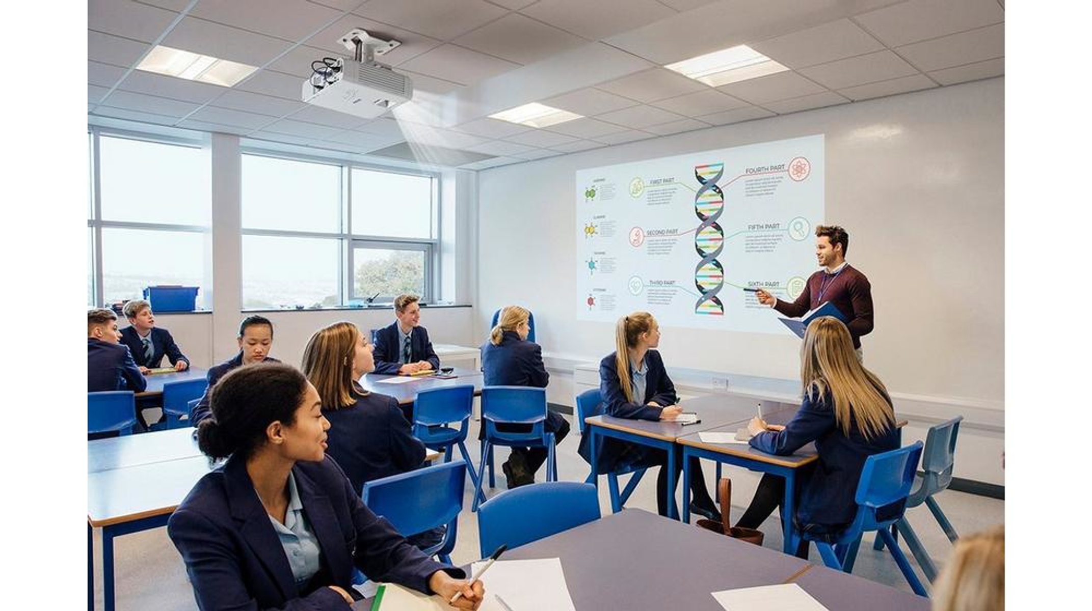 Klasa ze studentami i nauczycielem. Nauczyciel wskazuje ekran z informacjami.