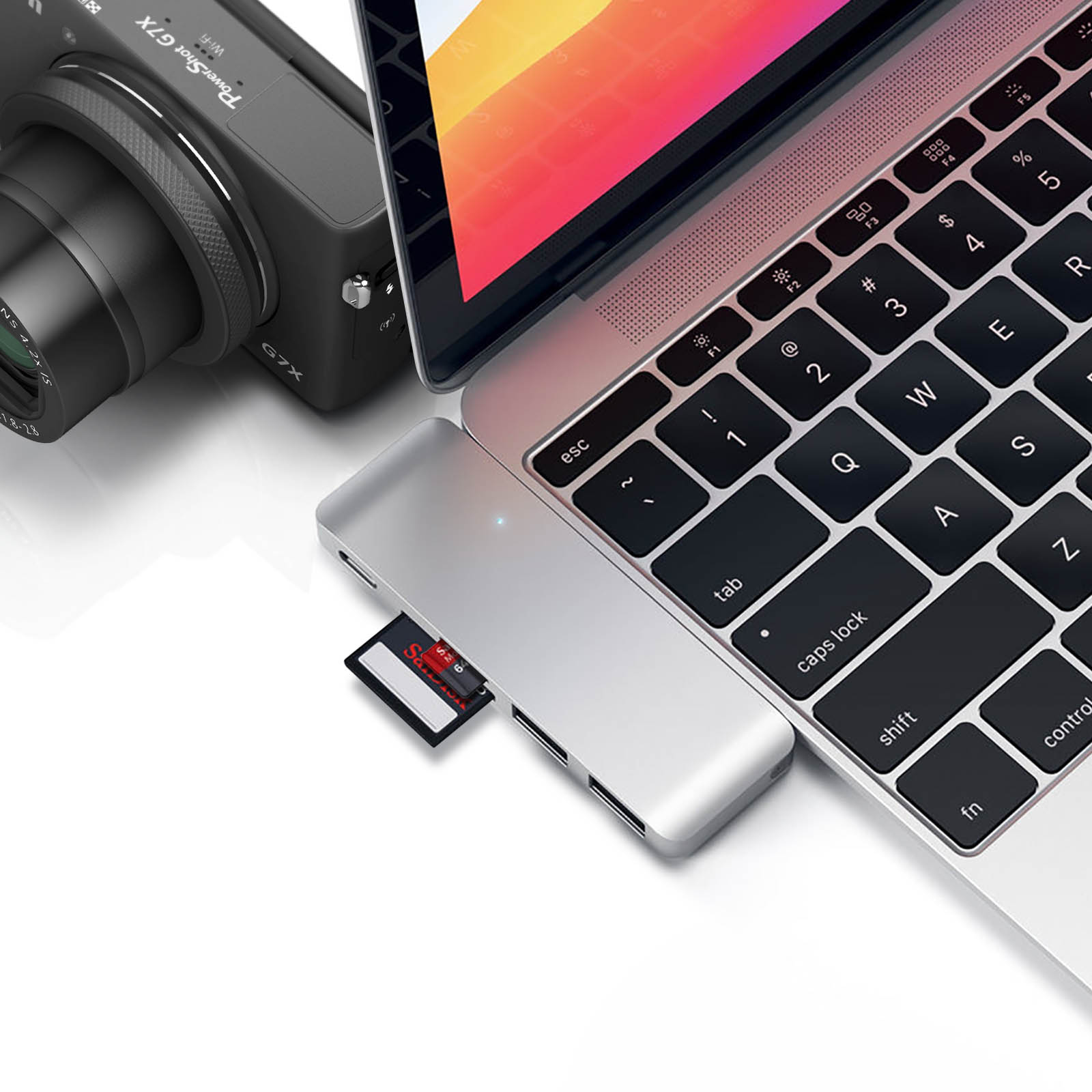 Laptop, Hub mit SD-Karte und Kamera auf weißer Oberfläche.