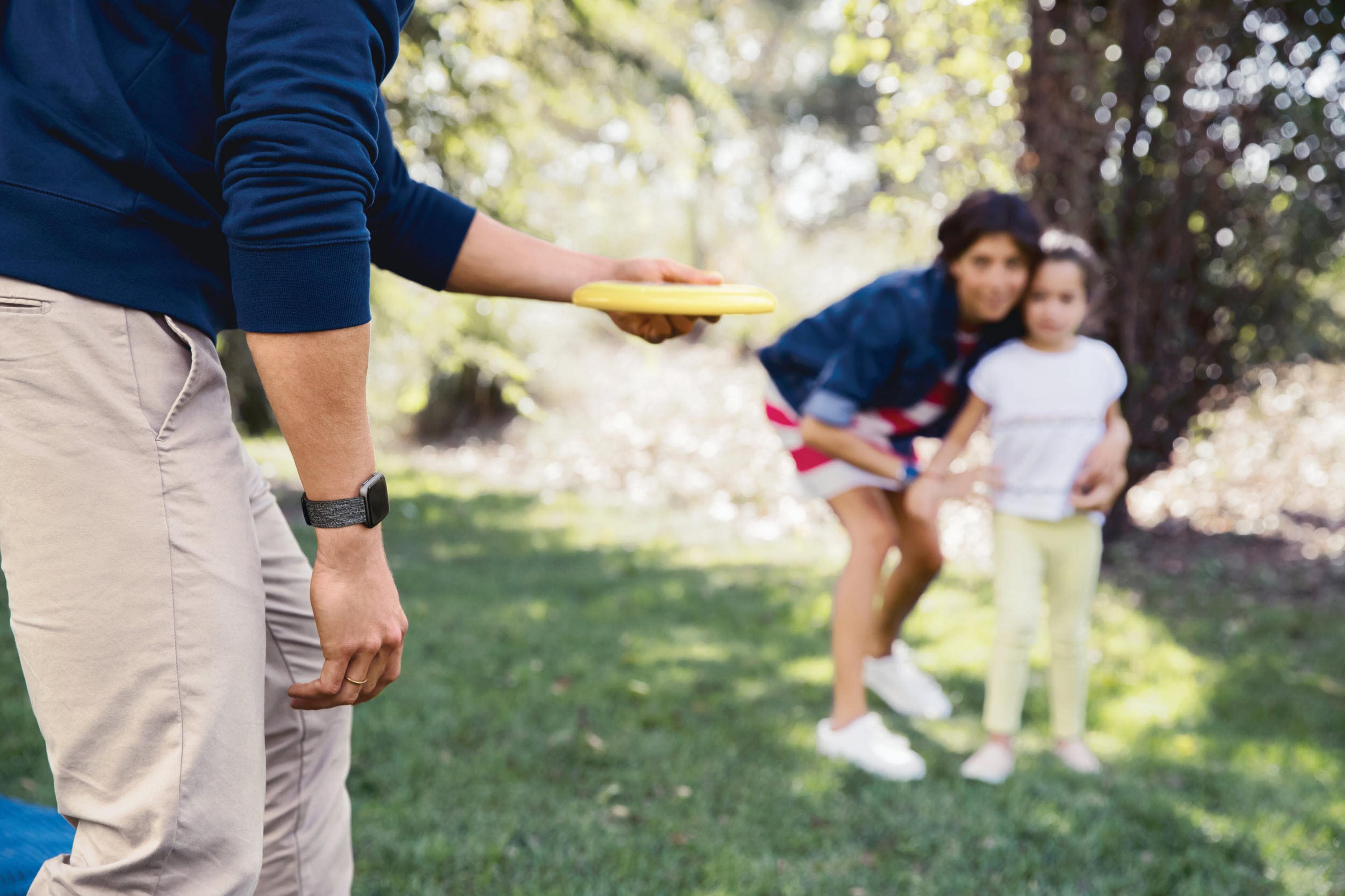 Ein Mann wirft eine gelbe Frisbeescheibe in Richtung einer Frau und eines Kindes in einem Park.