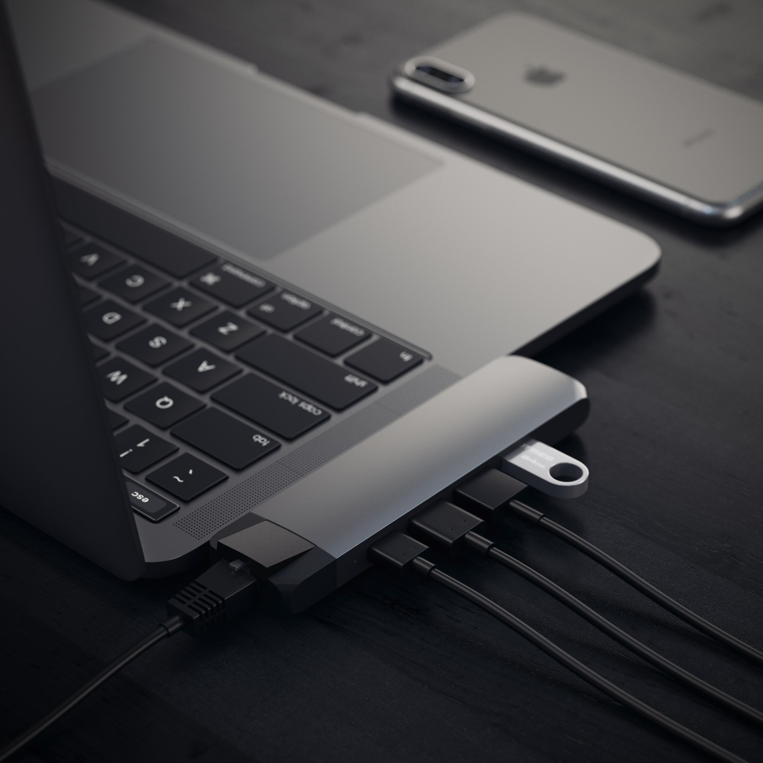 Laptop with a hub connected, with phone on a black wooden table.