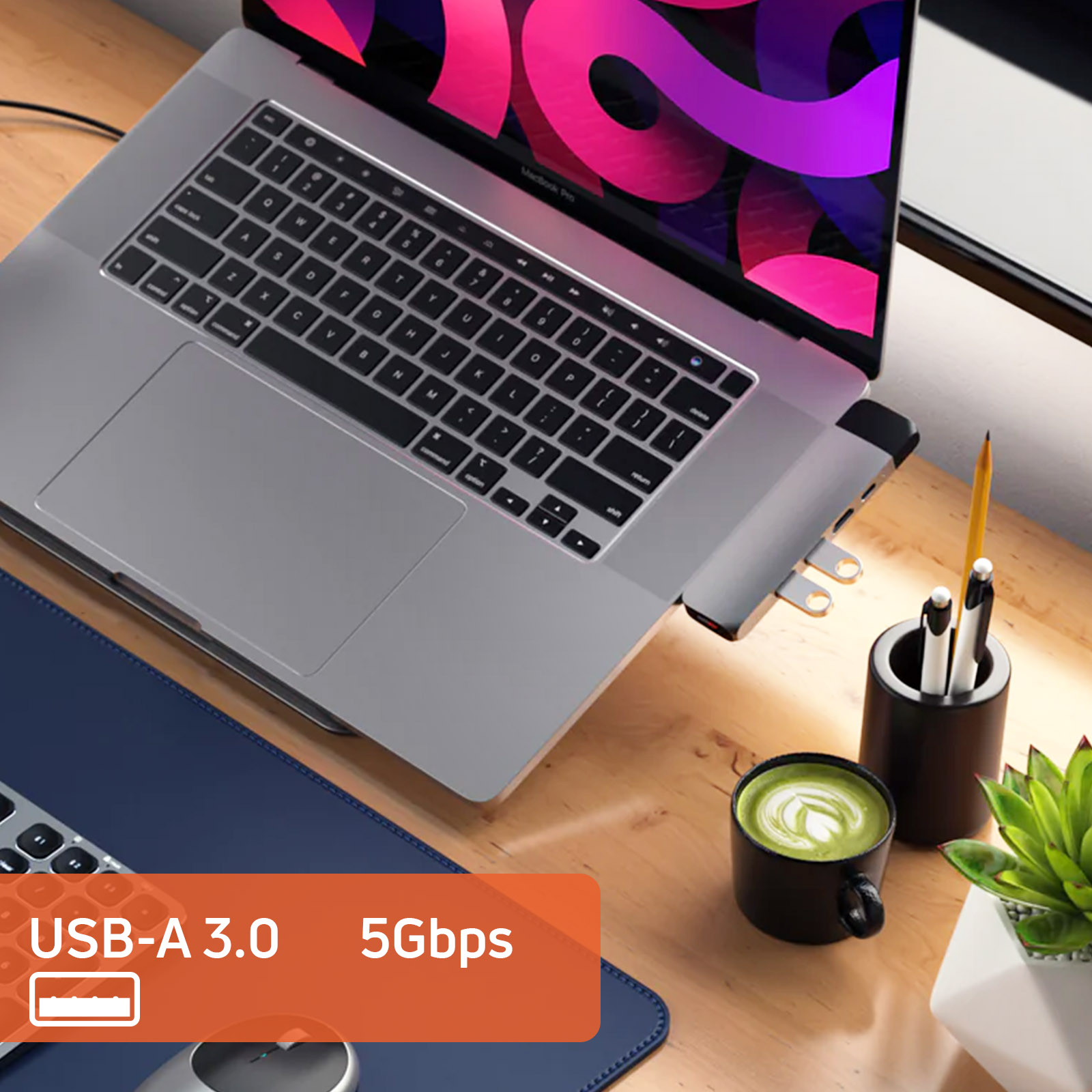 Een laptop met een USB-hub, koffiekopje, pennenhouder en plant op een bureau.