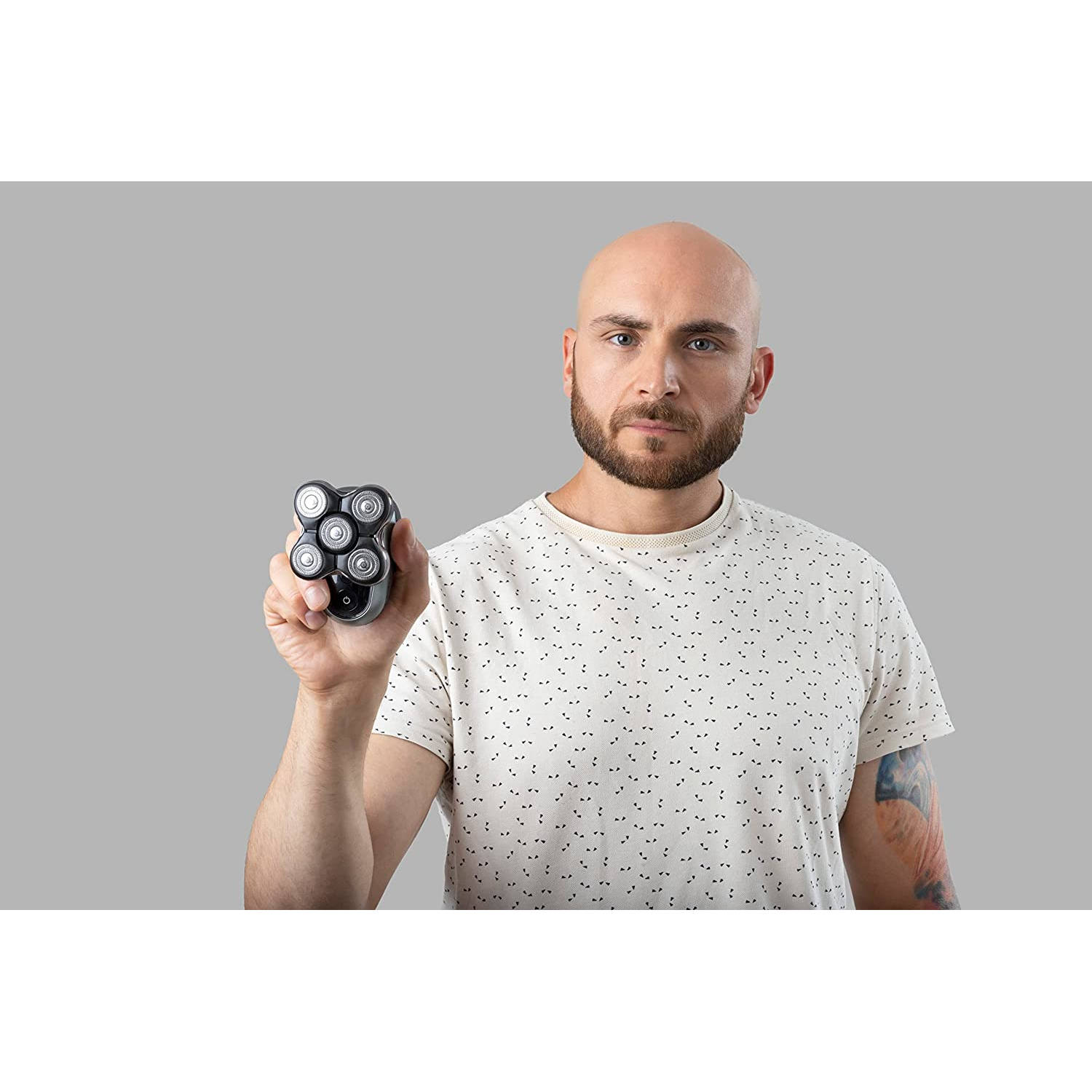 Ein kahler Mann mit Bart hält einen schwarzen Elektrorasierer.