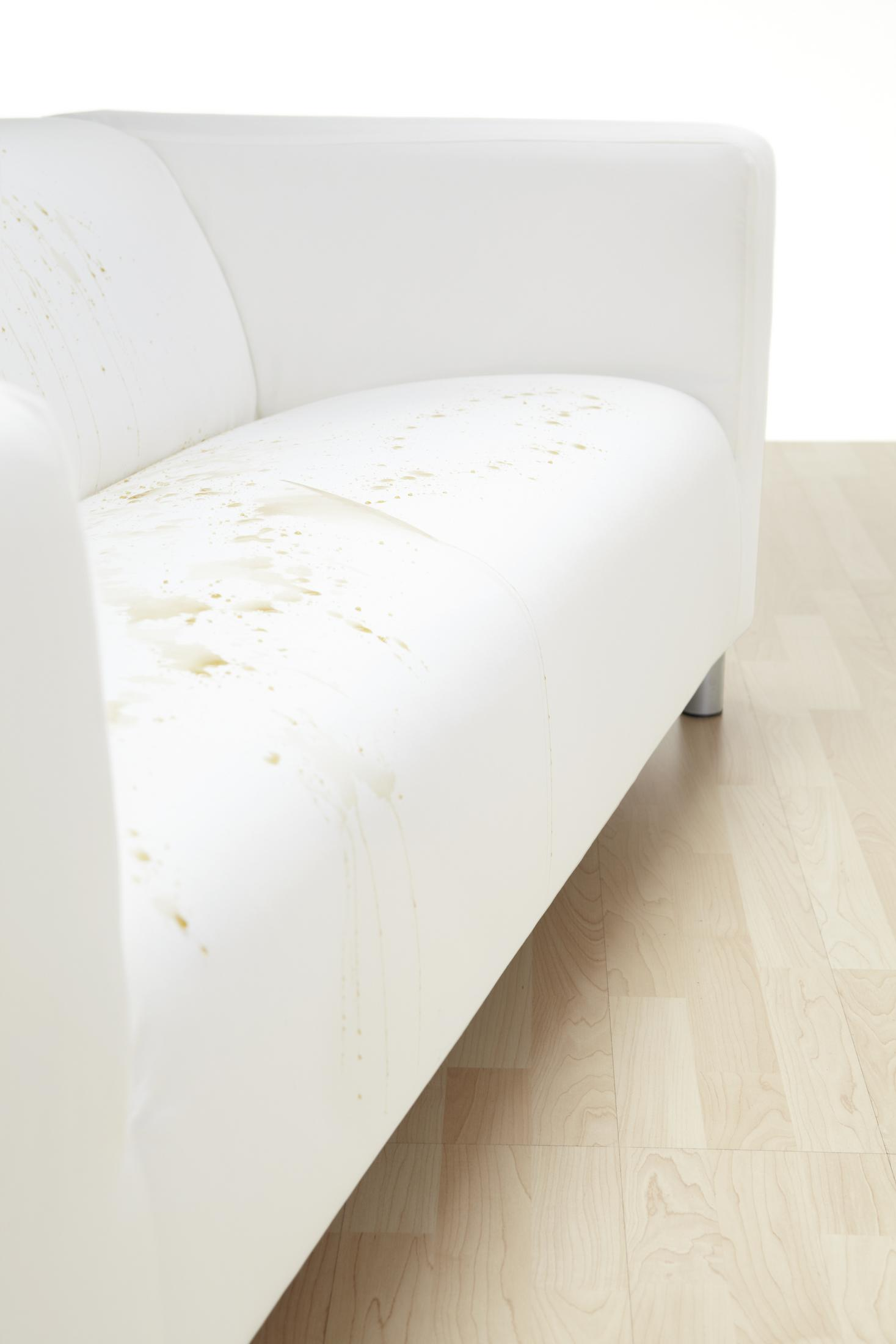 Ein weißes Sofa mit Flecken auf dem Kissen, auf einem hellen Holzboden. Das Sofa ist im Vordergrund.