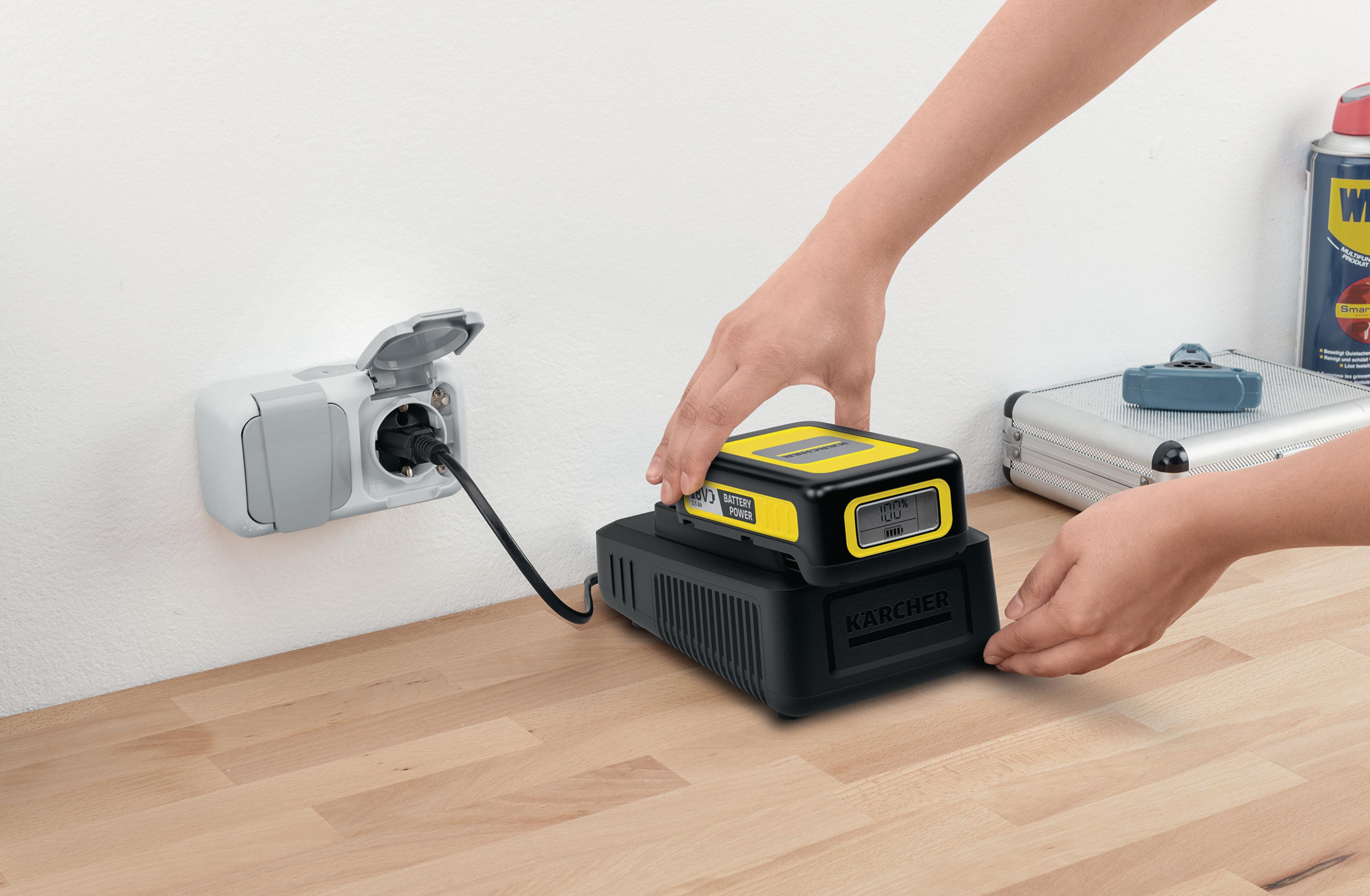 Osoba umieszcza akumulator w stacji ładującej. Biała ściana z gniazdem.