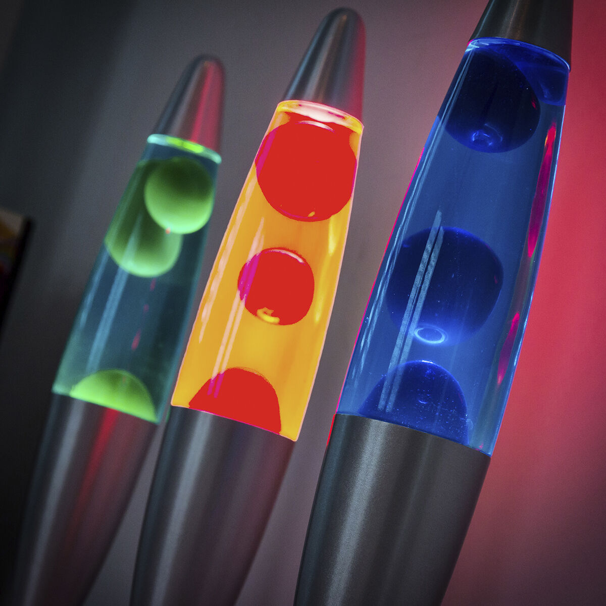 Trzy lampy lawowe z czerwoną, pomarańczową i niebieską lawą w środku, na ciemnym tle.