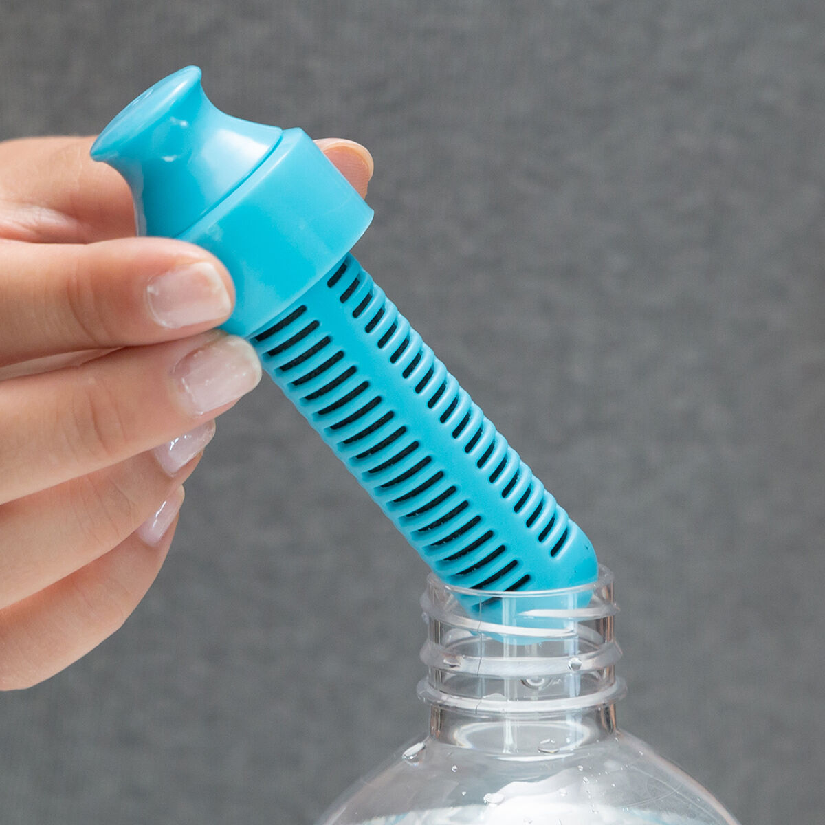 Una persona inserisce un filtro per l'acqua blu in una bottiglia trasparente. Sfondo grigio.