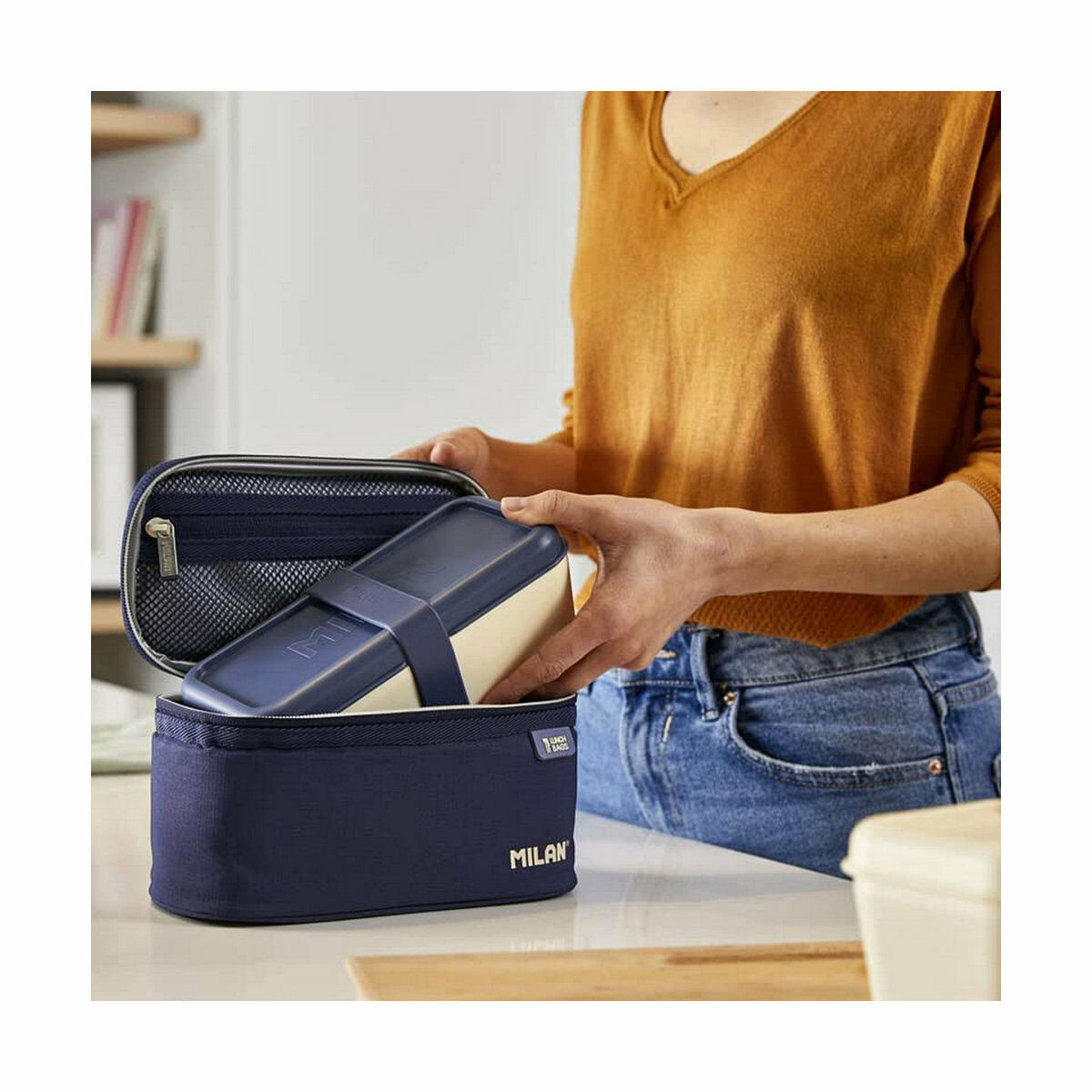Eine Person öffnet eine Milan-Lunchbox. Sie ist marineblau mit einem beigen Fach. Der Hintergrund ist eine Küche.