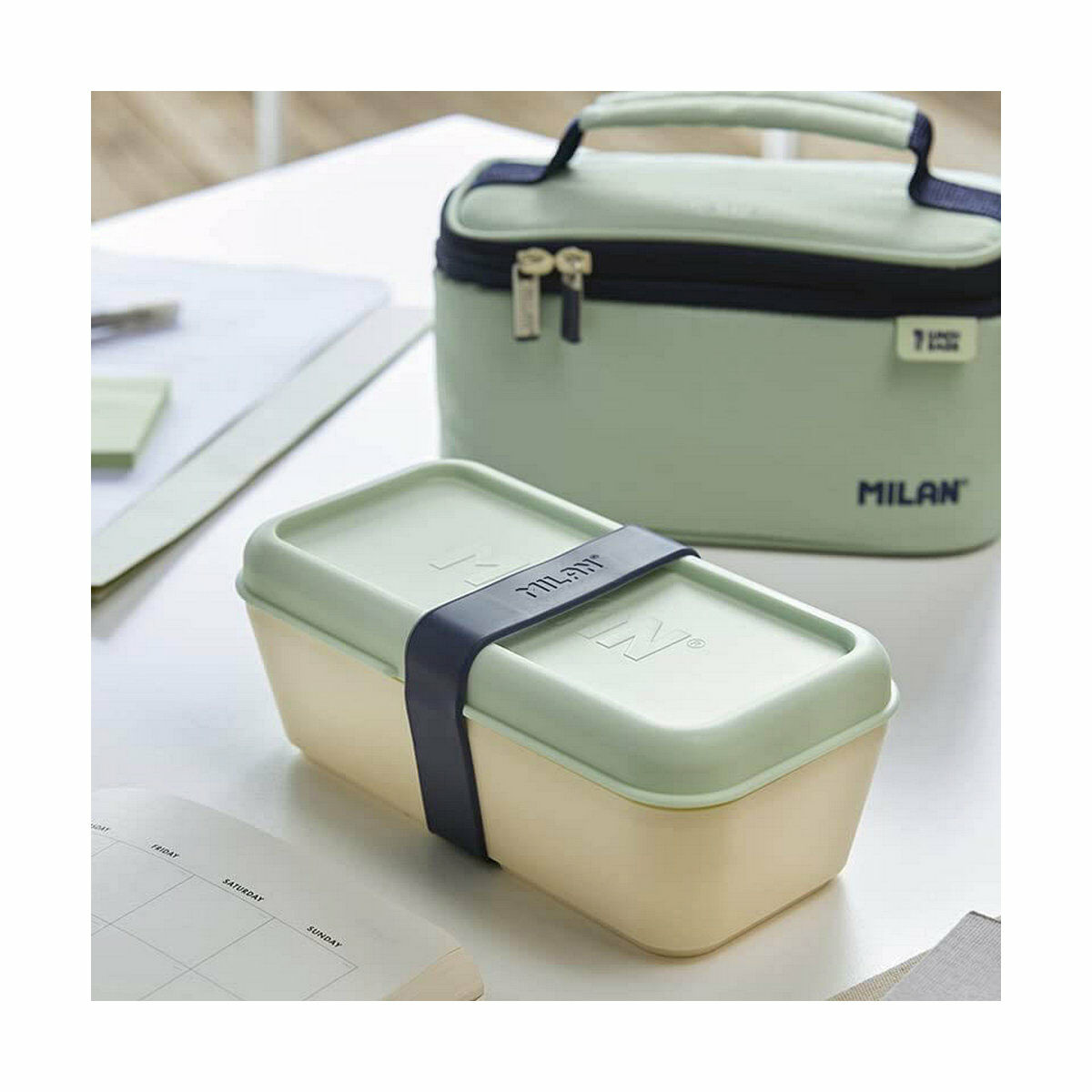 Lunchbox mit hellgrüner Lunchtasche auf einem weißen Tisch mit einem Kalender.