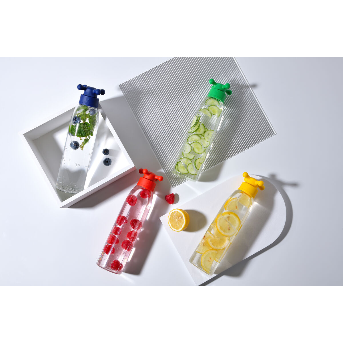 Vier Wasserflaschen mit Fruchtscheiben. Blaubeeren, Gurken, Himbeeren und Zitronen sind sichtbar. Weißer Hintergrund.
