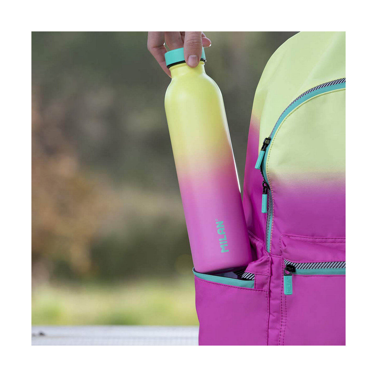 Eine Wasserflasche wird in eine Rucksacktasche gesteckt. Die Flasche ist gelb und rosa.