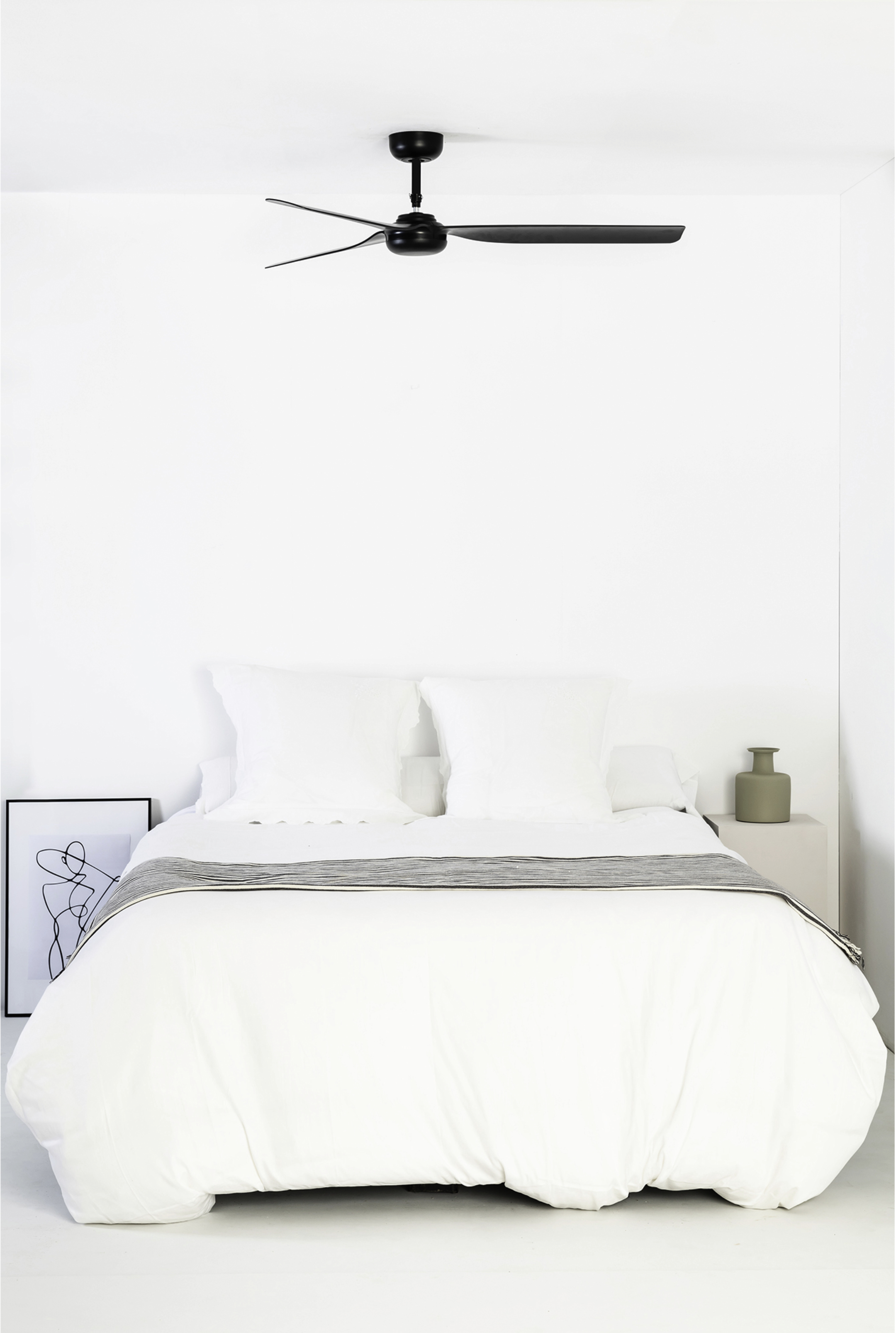 Camera da letto con biancheria da letto bianca, ventilatore a soffitto nero e comodino.