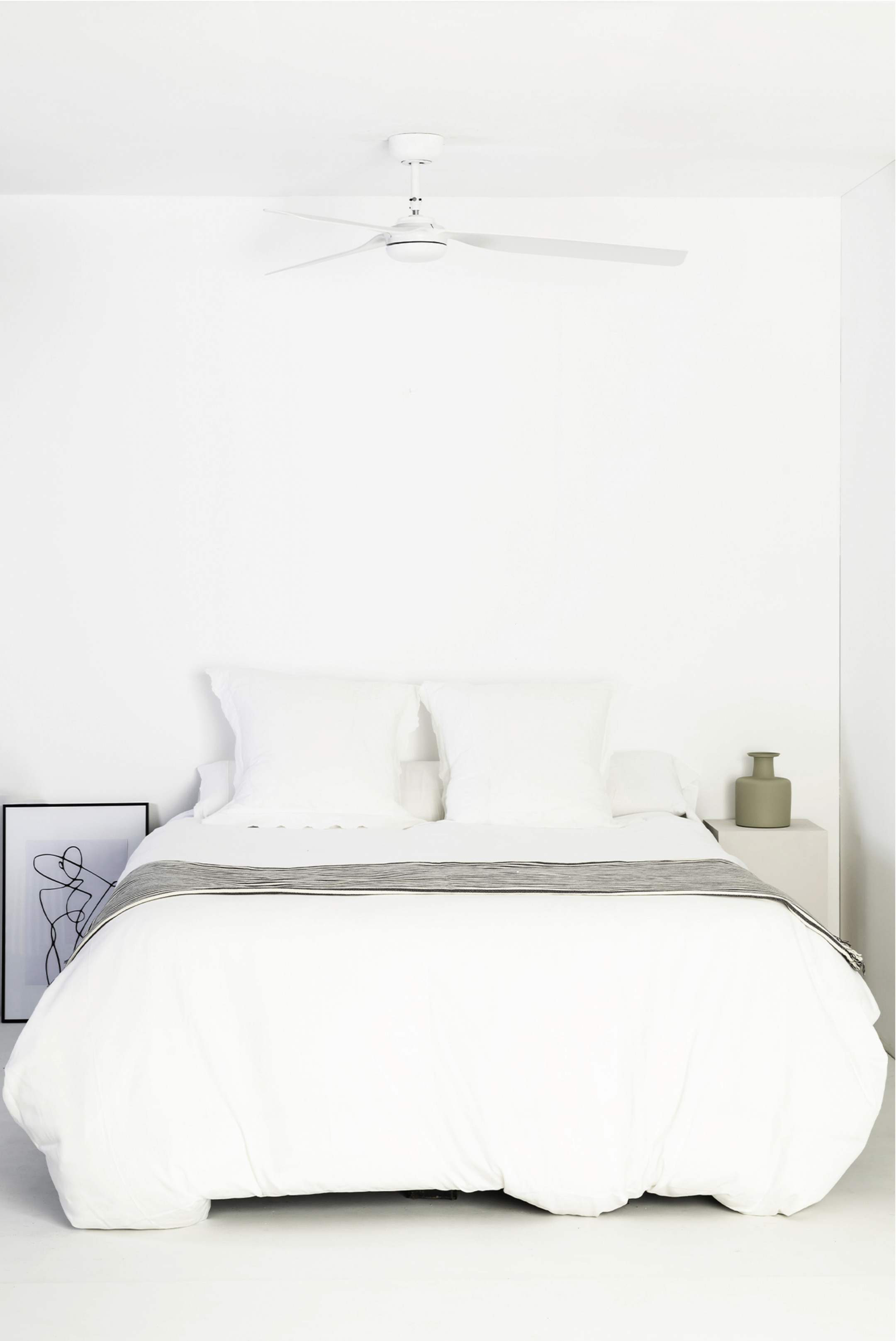 Camera da letto con arredi bianchi. Letto con biancheria da letto bianca, opere d'arte e ventilatore a soffitto.