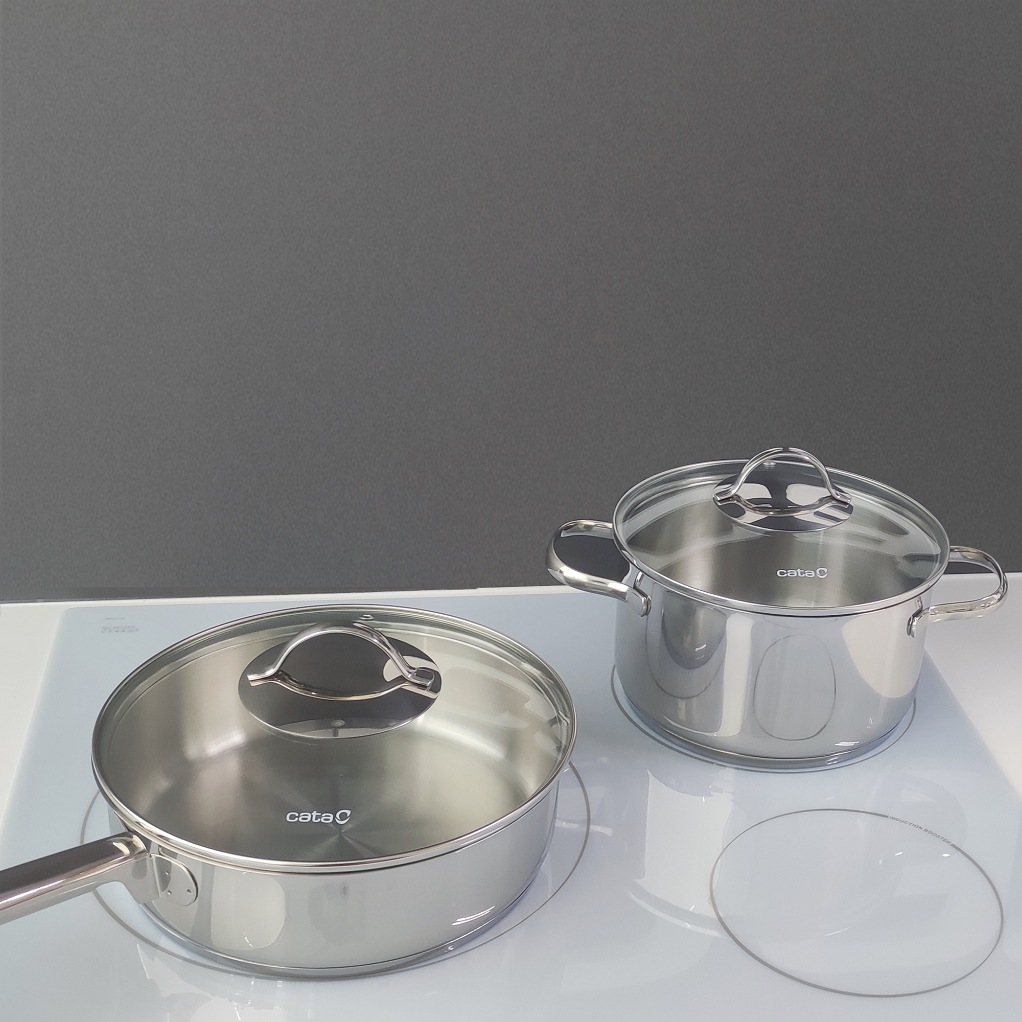 Utensilios de cocina de acero inoxidable sobre una encimera blanca. Dos ollas y una sartén visibles.