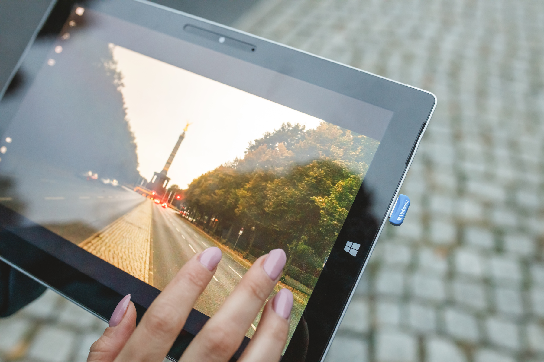 Tablet wyświetlający scenę uliczną, trzymany w dłoni, z dołączonym niebieskim pendrivem.