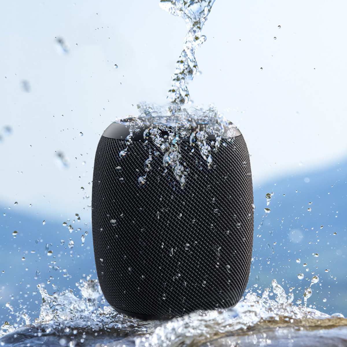 Schwarzer Lautsprecher, auf den Wasser spritzt, vor dem Hintergrund von Bergen.