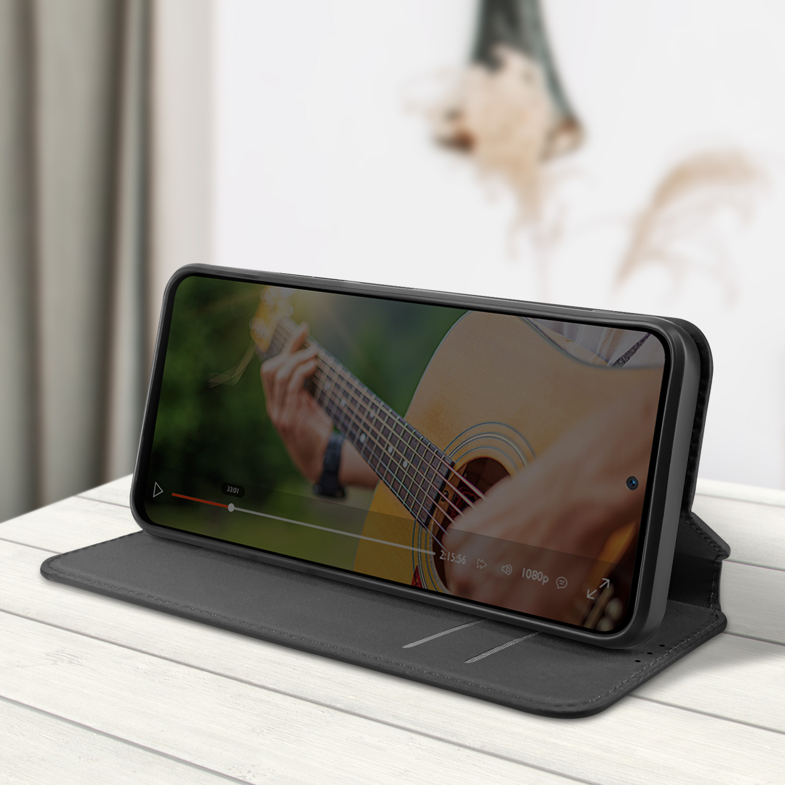 Un smartphone en una funda tipo folio gris oscuro. En la pantalla hay un vídeo de una persona tocando la guitarra.