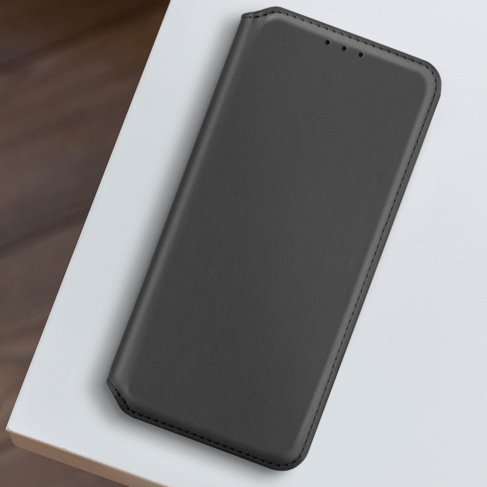 Funda de teléfono de cuero negro sobre una superficie blanca. Bordes cosidos, diseño sencillo.