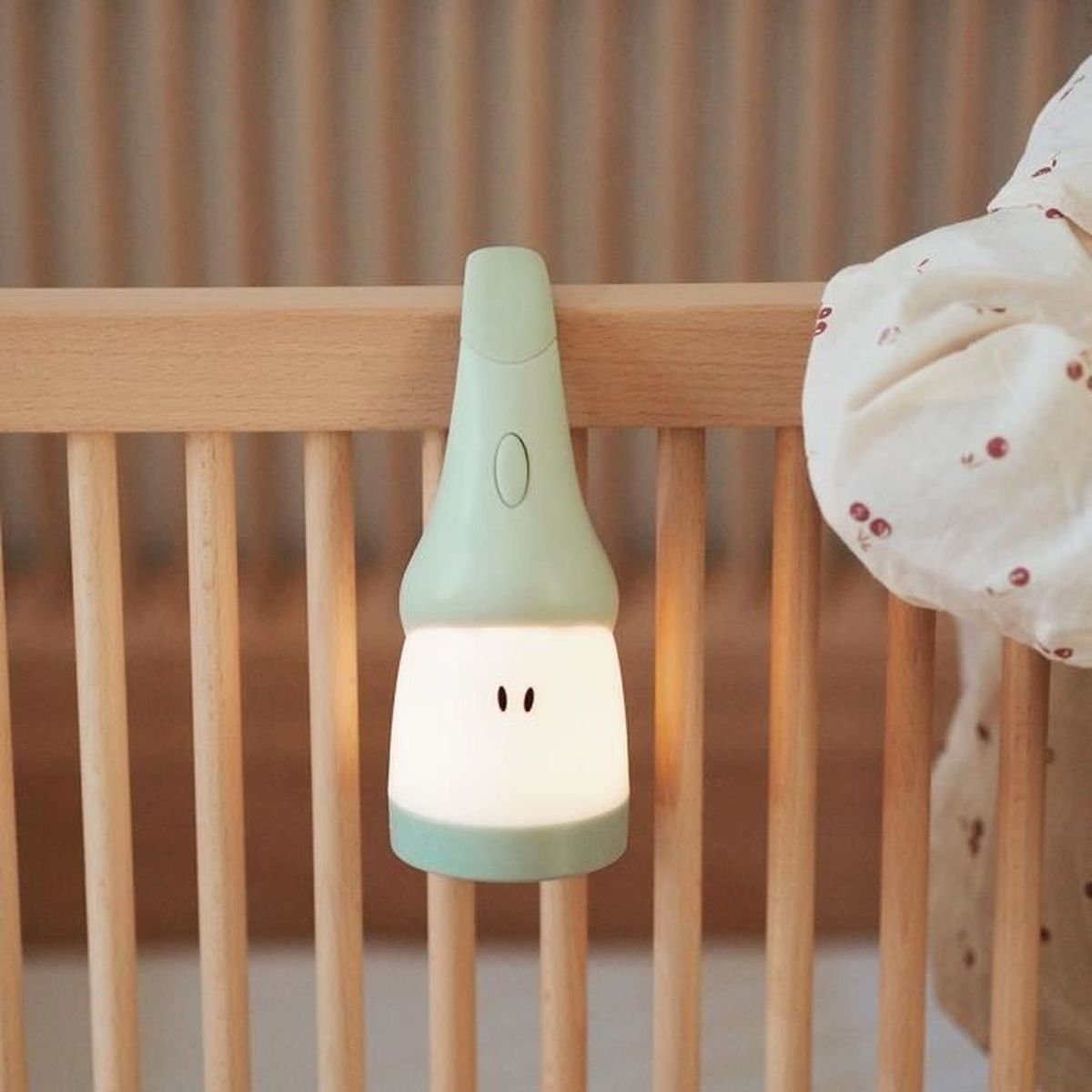 Ein grünes Babynachtlicht an einem Kinderbett. Es hat ein Gesicht und ist eingeschaltet. Licht wird emittiert.