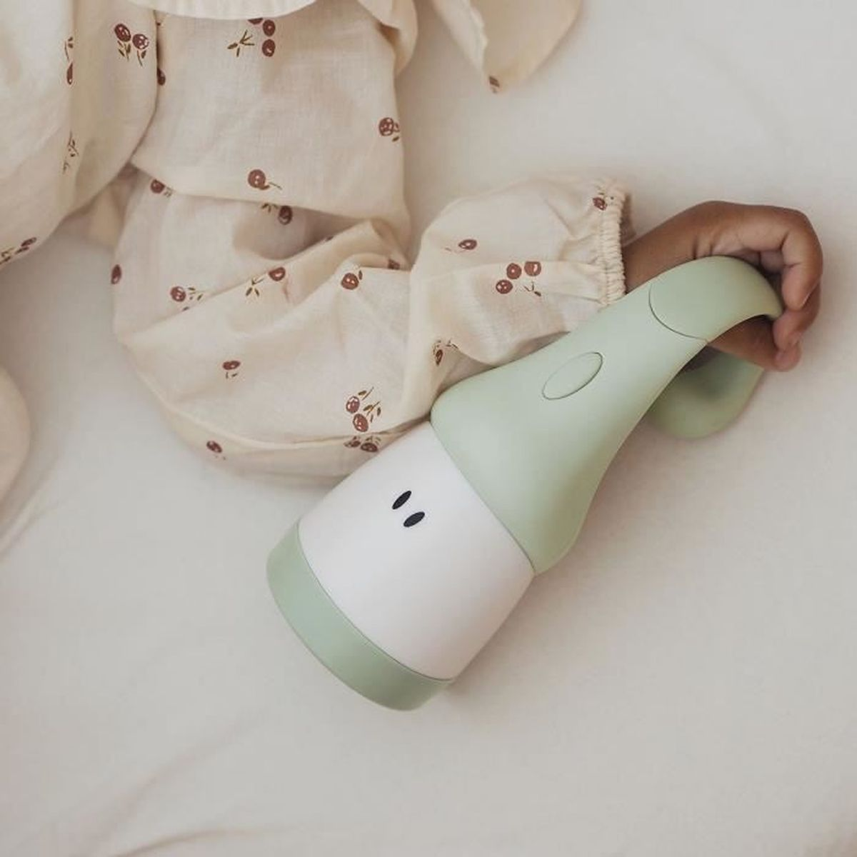 Baby hält ein grün-weißes Spielzeug. Beige Schlafanzug, heller Hintergrund.