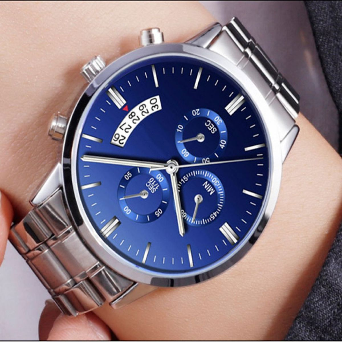 Nahaufnahme einer blauen Zifferblattuhr mit silbernem Armband am Handgelenk.