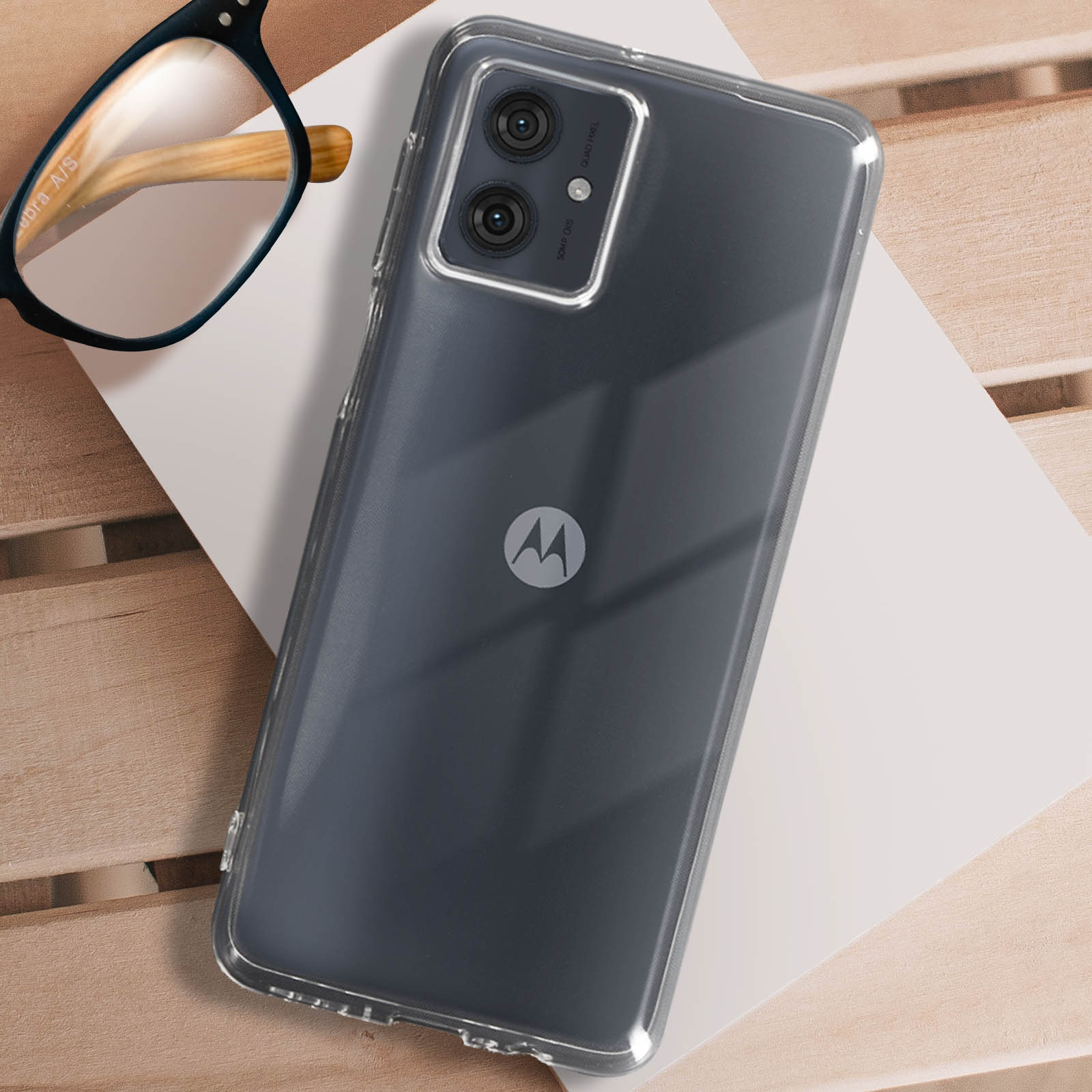 Uno smartphone grigio con custodia trasparente e due fotocamere, appoggiato su un tavolo di legno con occhiali.