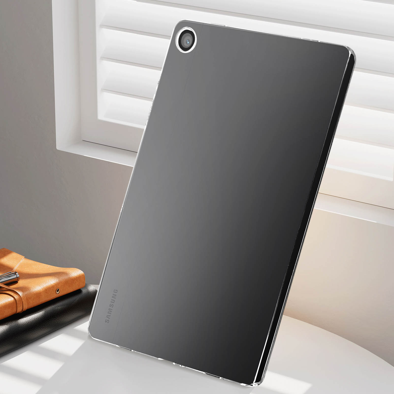 Ein schwarzes Tablet auf weißer Oberfläche, in der Nähe eines Fensters. Es hat eine Kamera und das Samsung-Logo.