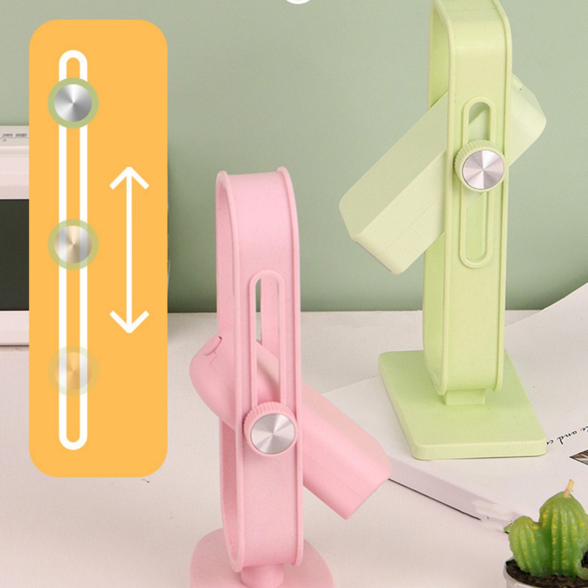 Zwei kleine Ventilatoren, einer rosa, einer grün, auf einem Schreibtisch. Ein Bedienfeld ist links.