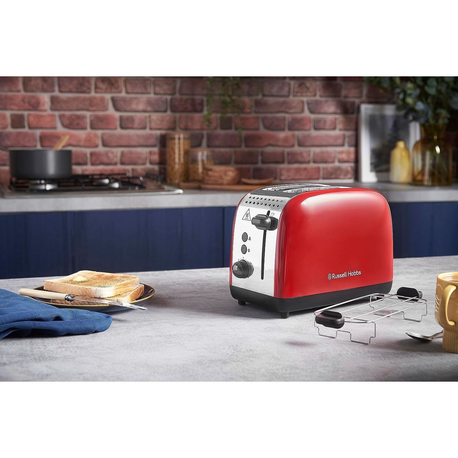 Roter Toaster mit Chromdetails auf einer grauen Arbeitsplatte neben Toast und einer gelben Tasse.