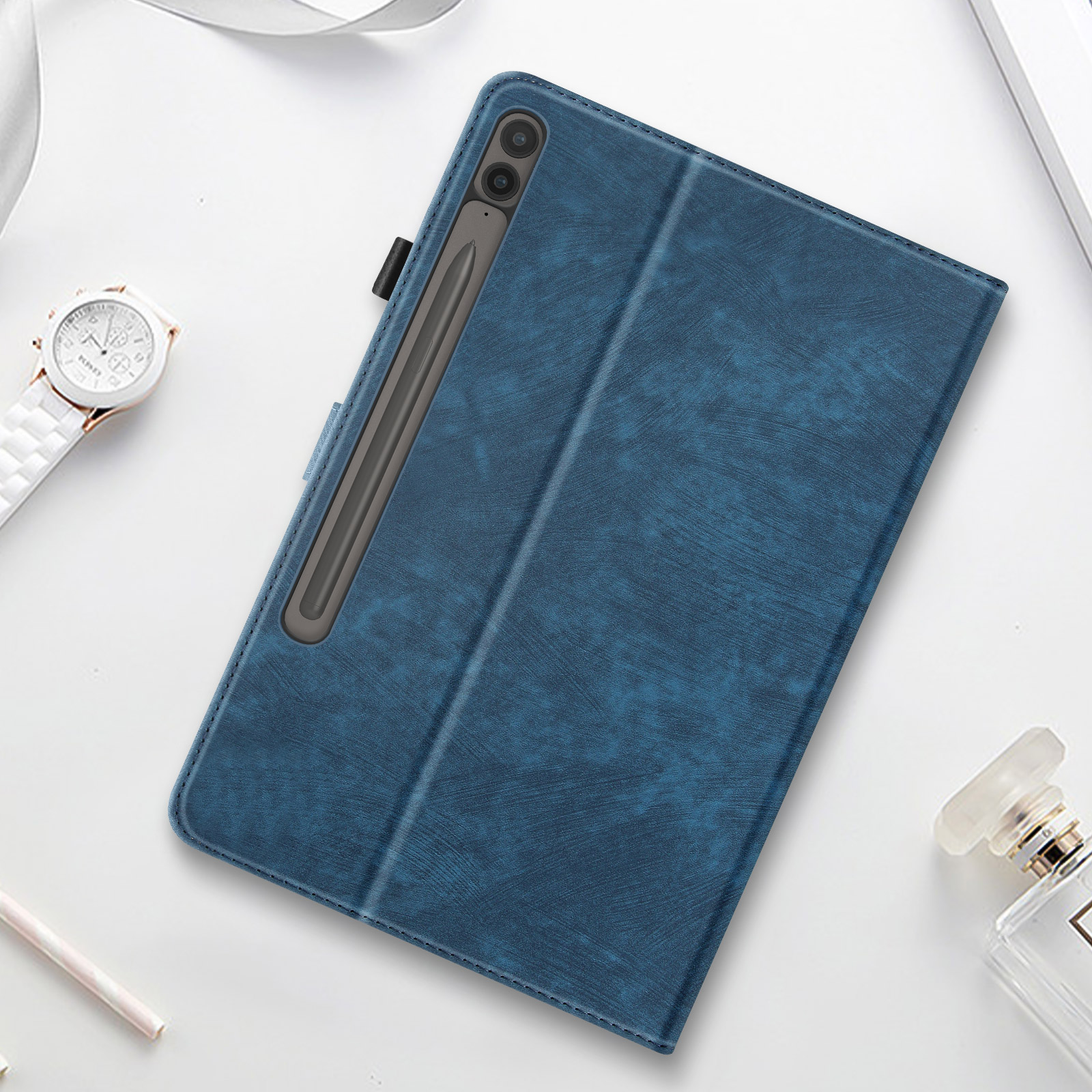 Custodia blu per tablet con pennino. Superficie bianca con orologio e profumo.