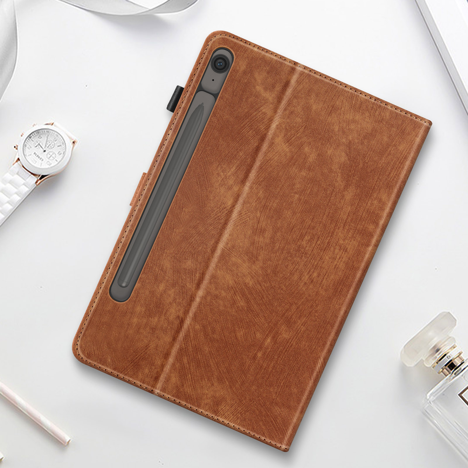 Custodia per tablet marrone con stilo. Orologio bianco, profumo e matita su superficie bianca.
