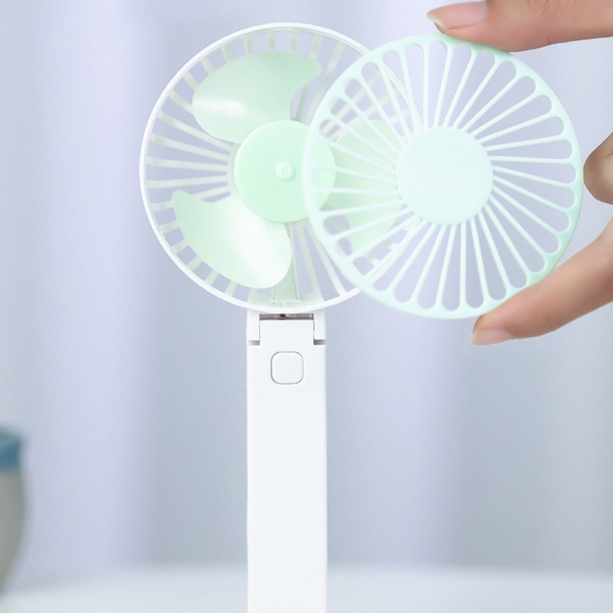 Ein weißer Handventilator ist geöffnet und zeigt die Flügel. Ein anderer Teil wird gehalten.