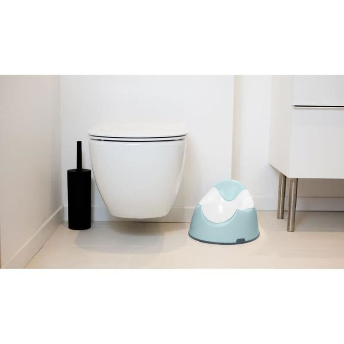 Eine weiße Toilette und ein tealfarbener Töpfchen in einem Badezimmer. Schwarze Bürste.