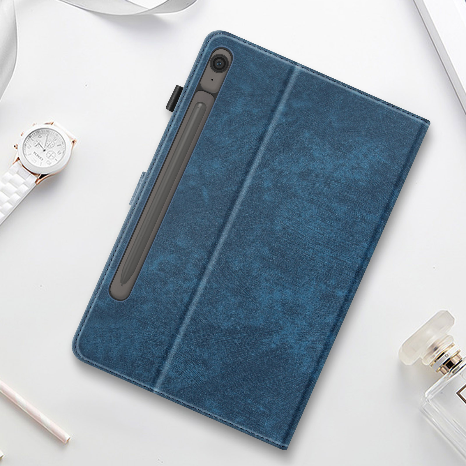 Una custodia blu per tablet con un portapenne. Un orologio bianco e un flacone di profumo sono sul lato.