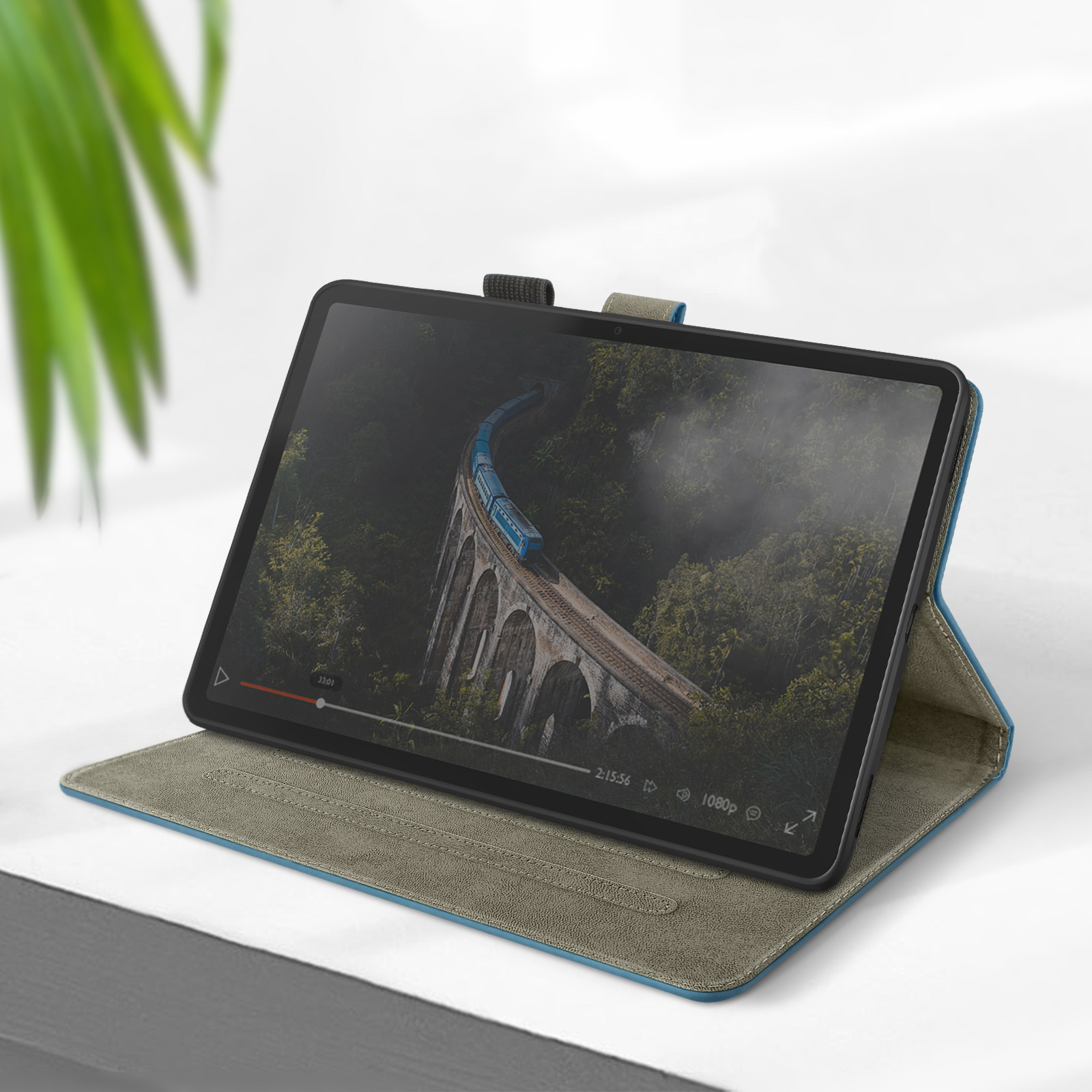 Tablet in custodia, mostra un video di un ponte. Custodia verde e blu, su superficie bianca.