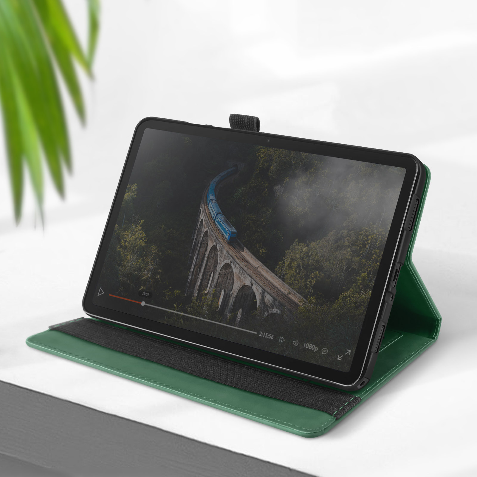 Tablet in una custodia verde che mostra una scena di ponte. Bordi neri, in piedi. Superficie bianca.