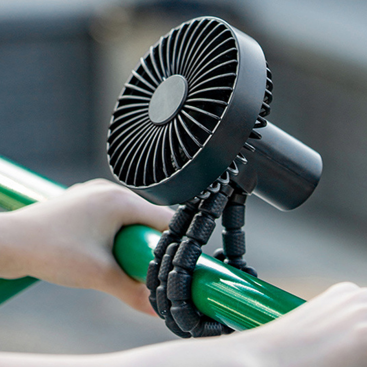 Schwarzer tragbarer Ventilator an einer grünen Stange befestigt. Hände halten die Stange.