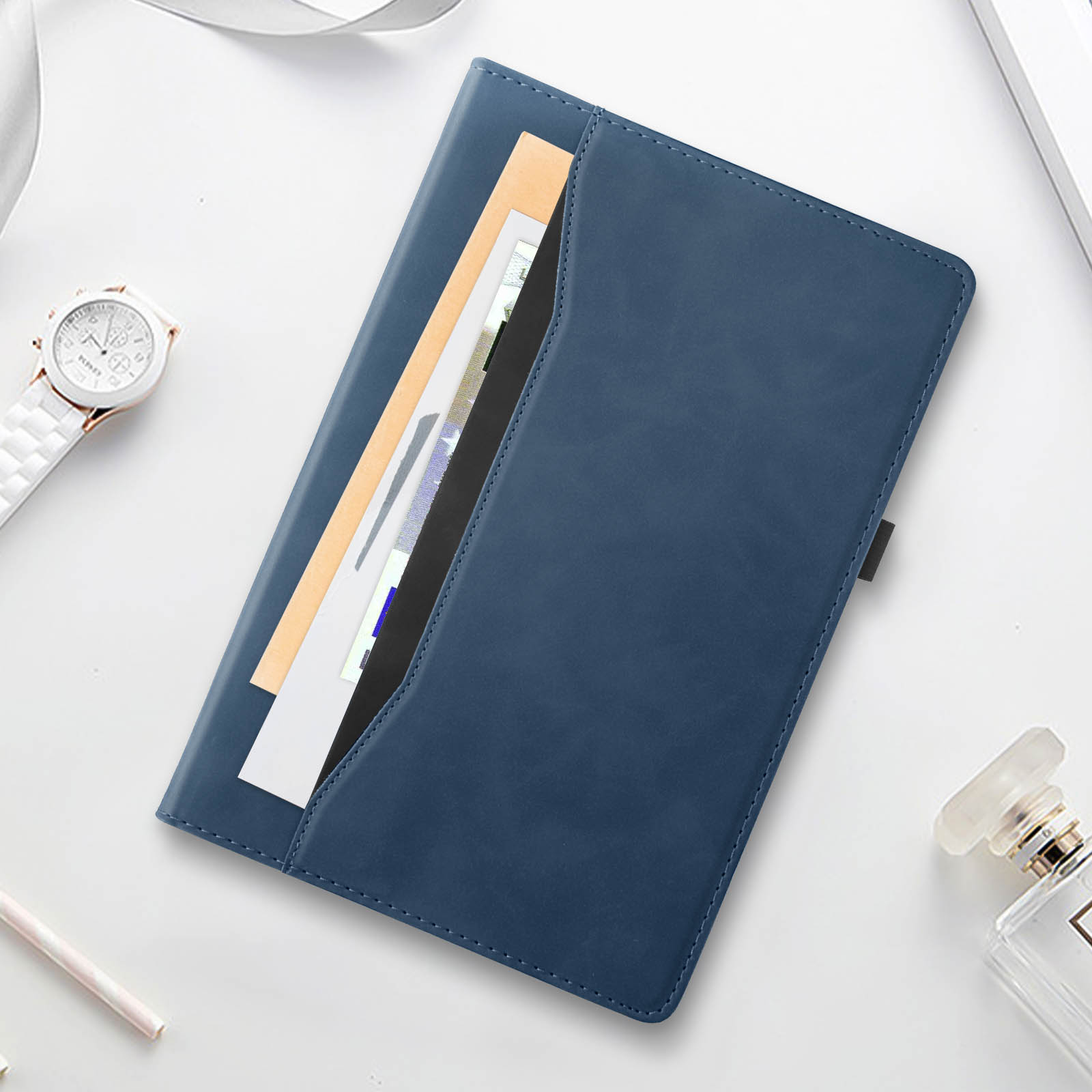 Custodia per tablet in pelle blu con documenti e un orologio su una superficie bianca.
