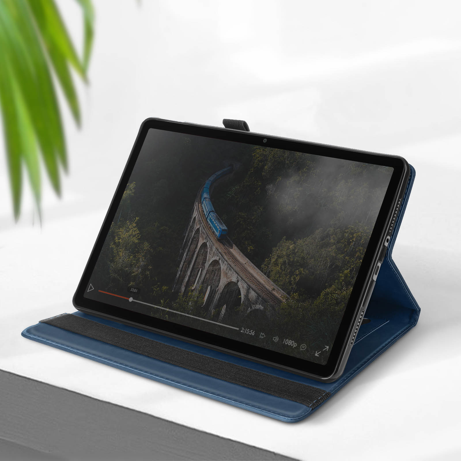 Tablet con video sullo schermo, cover blu. Superficie chiara e pianta verde visibili.
