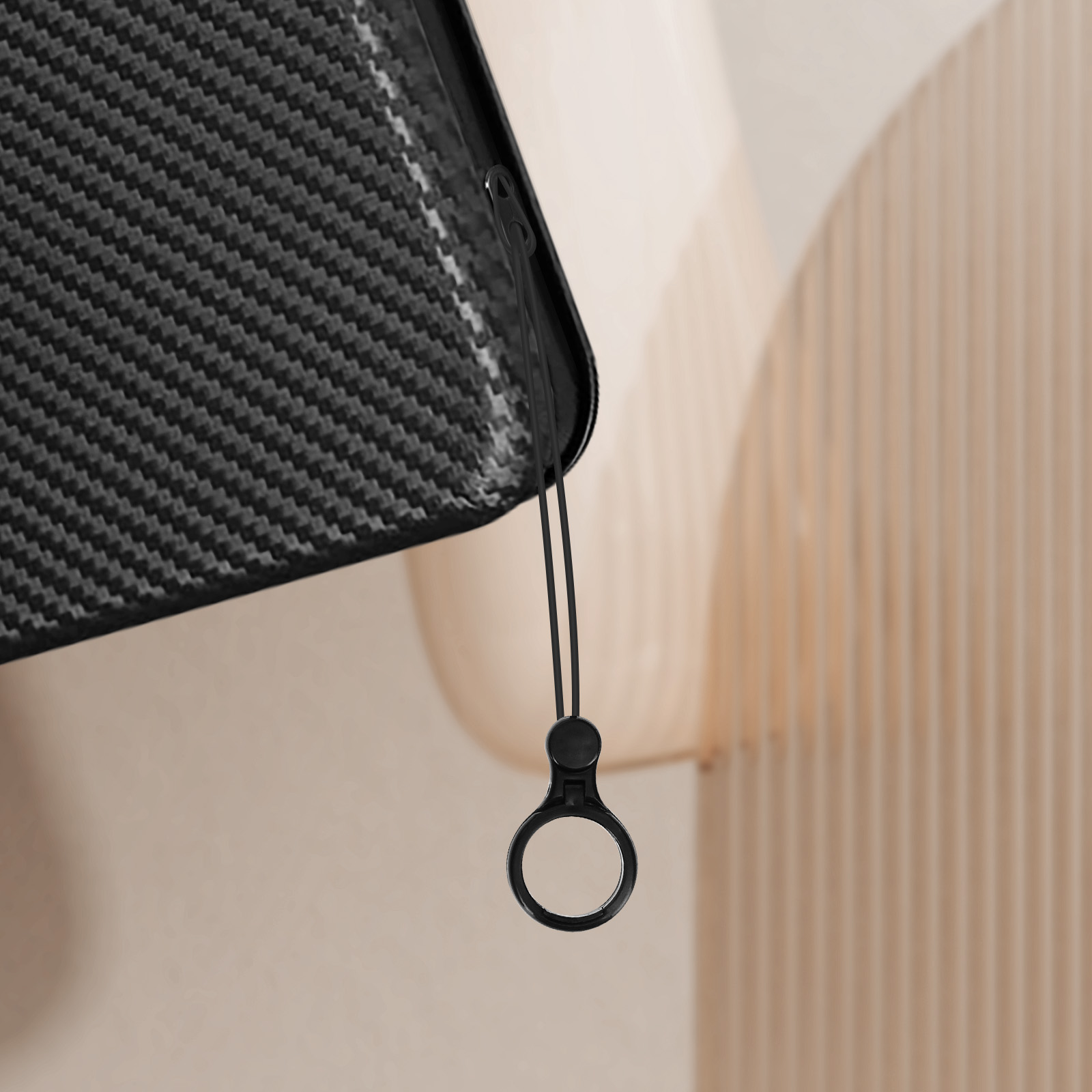 Una custodia per telefono nera con un cinturino, su sfondo beige.