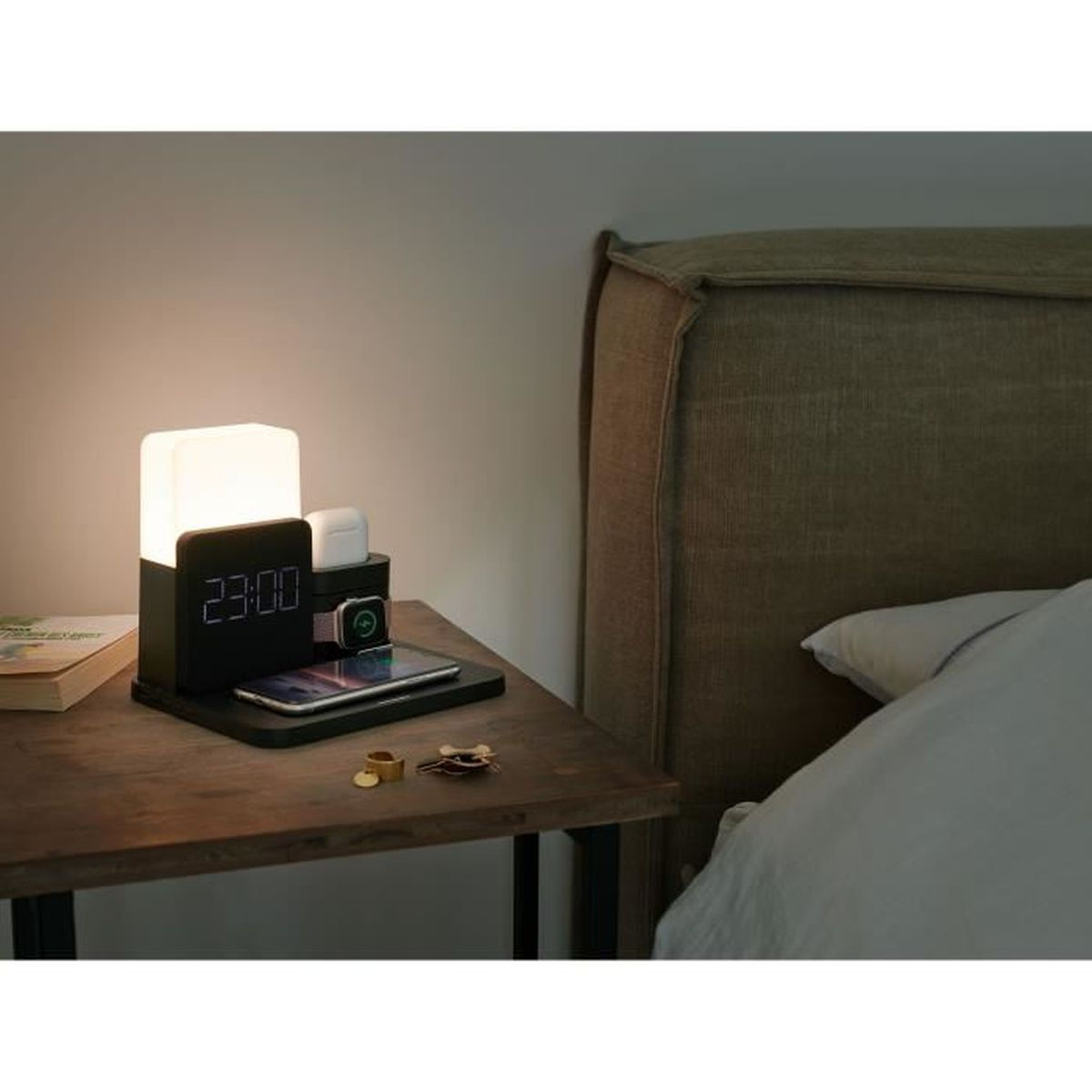 Czarna stacja ładująca przy łóżku z lampą, zegarem i urządzeniami. Drewniany stół, łóżko w tle.