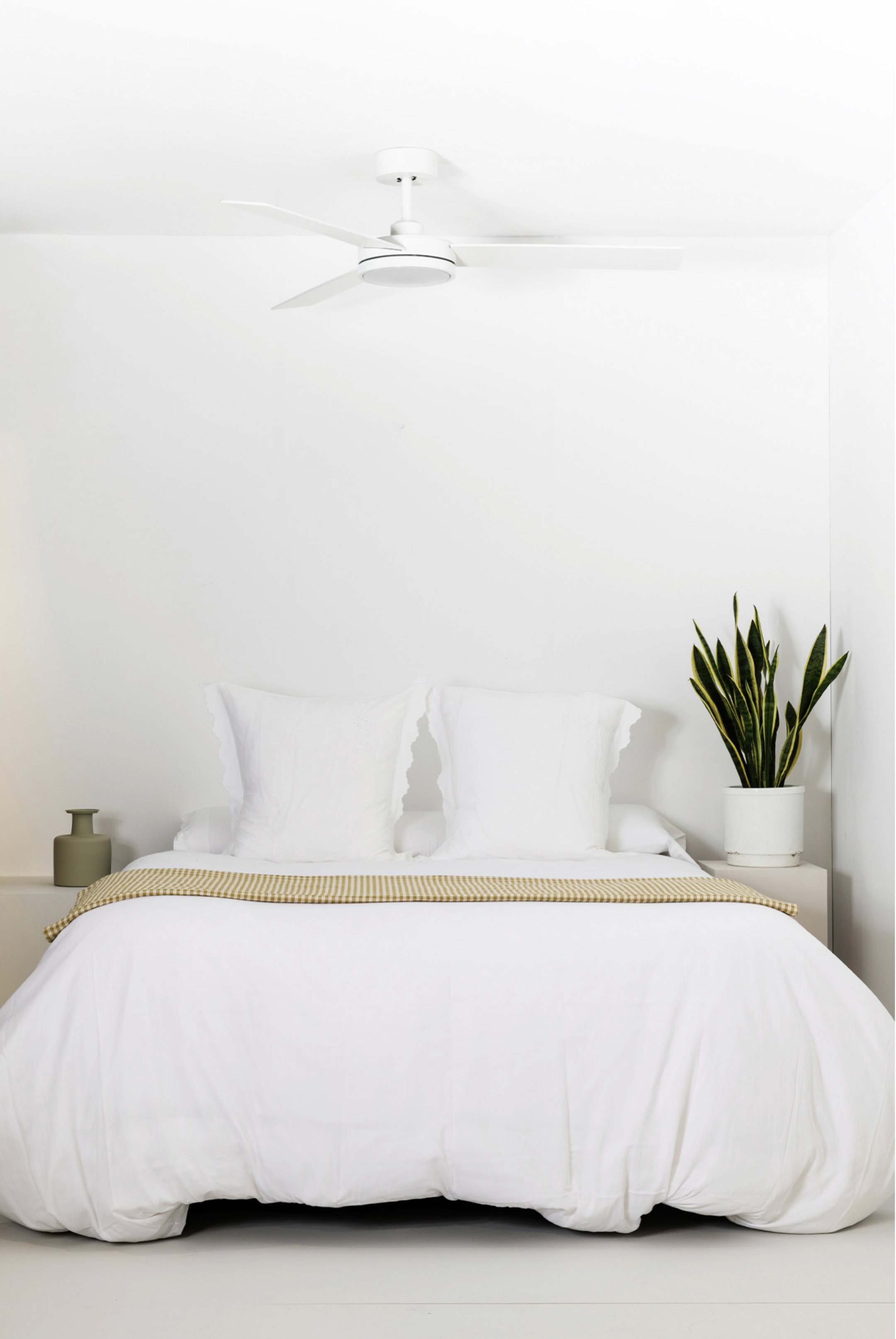 Camera da letto bianca con letto, due cuscini, una coperta e un ventilatore a soffitto.